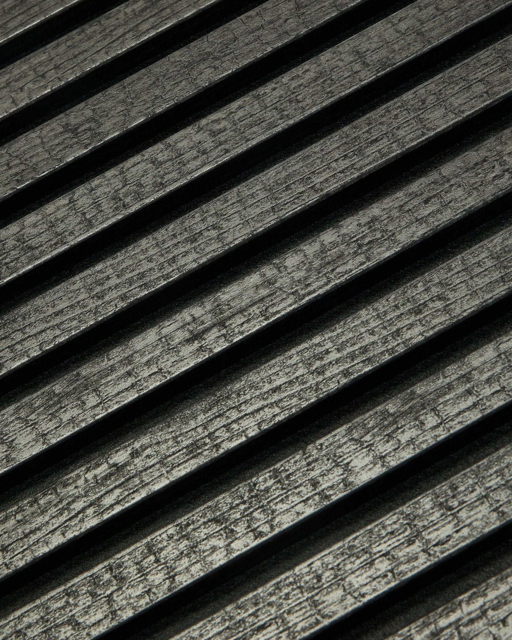 Grande plano do WoodUpp Rebel Akupanel em Charcoal (240x60 cm), mostrando black, com ripas acústicas ranhuradas dispostas na diagonal para melhorar a absorção sonora.