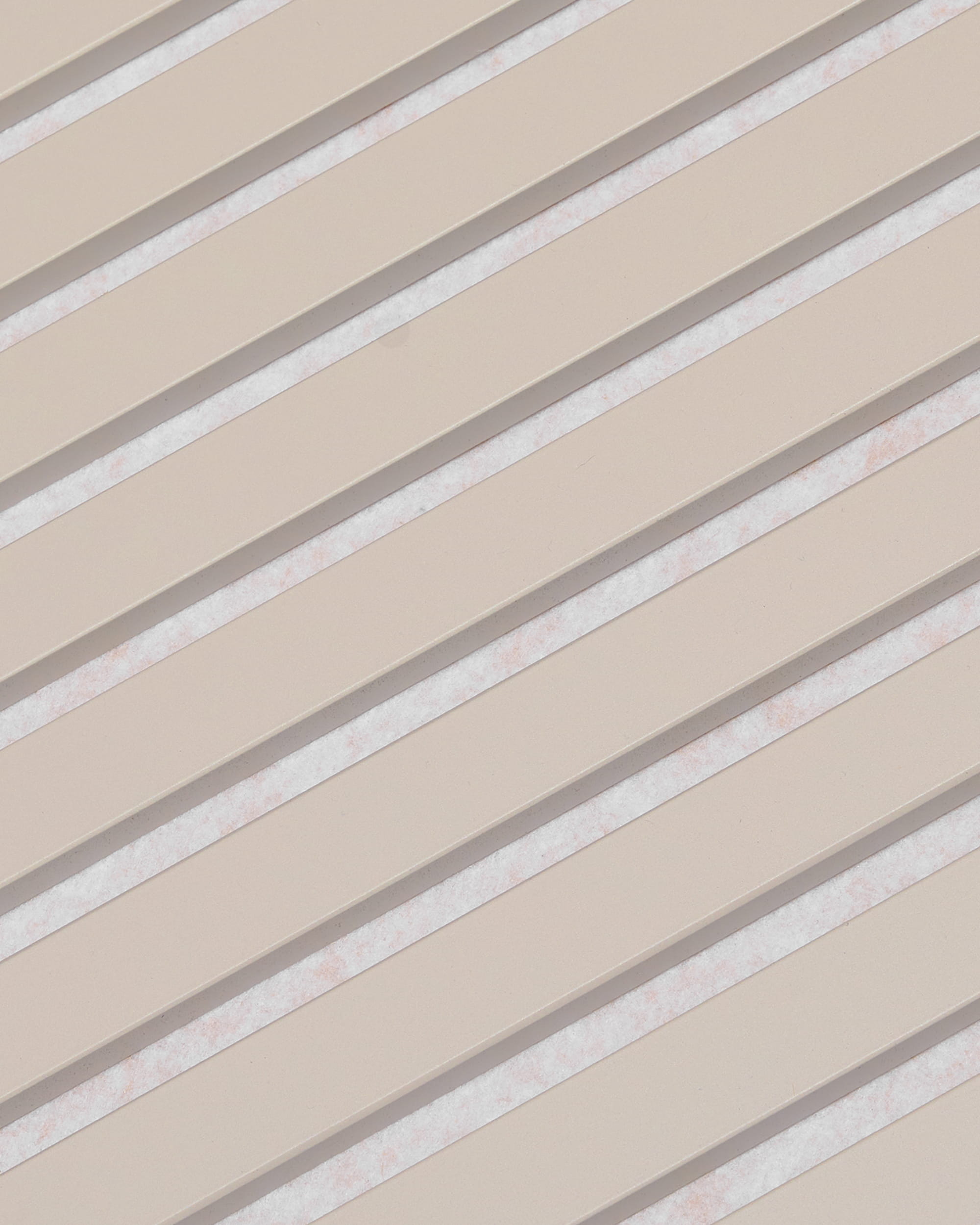 As ripas diagonais em bege, com espaços brancos, formam um padrão às riscas no painel acústico WoodUpp Akupanel, com acabamento em feltro Soft Linen Light Beige, 240 x 60 cm.