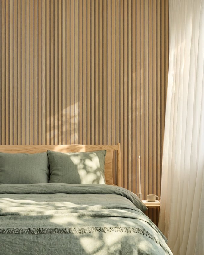 Quarto nórdico minimalista com uma parede WoodUpp Akupanel em carvalho Painel acústico, roupa de cama verde-sálvia, estrutura de cama em madeira e cortinas brancas translúcidas.