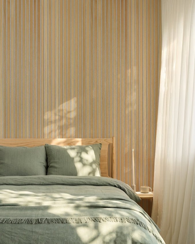 Quarto nórdico minimalista com roupa de cama verde-sálvia e uma parede acústica ripada WoodUpp Classic Oak Akupanel; a luz do sol cria sombras suaves na cama.