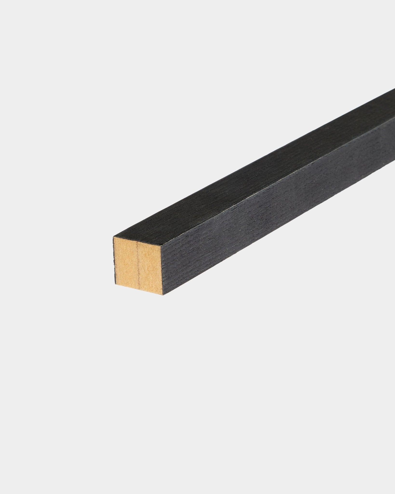 Lamela terminal WoodUpp Black em freixo, 2,2 cm, concebida para instalação Akupanel Painel acústico, assente sobre uma superfície branca com uma extremidade por acabar.
