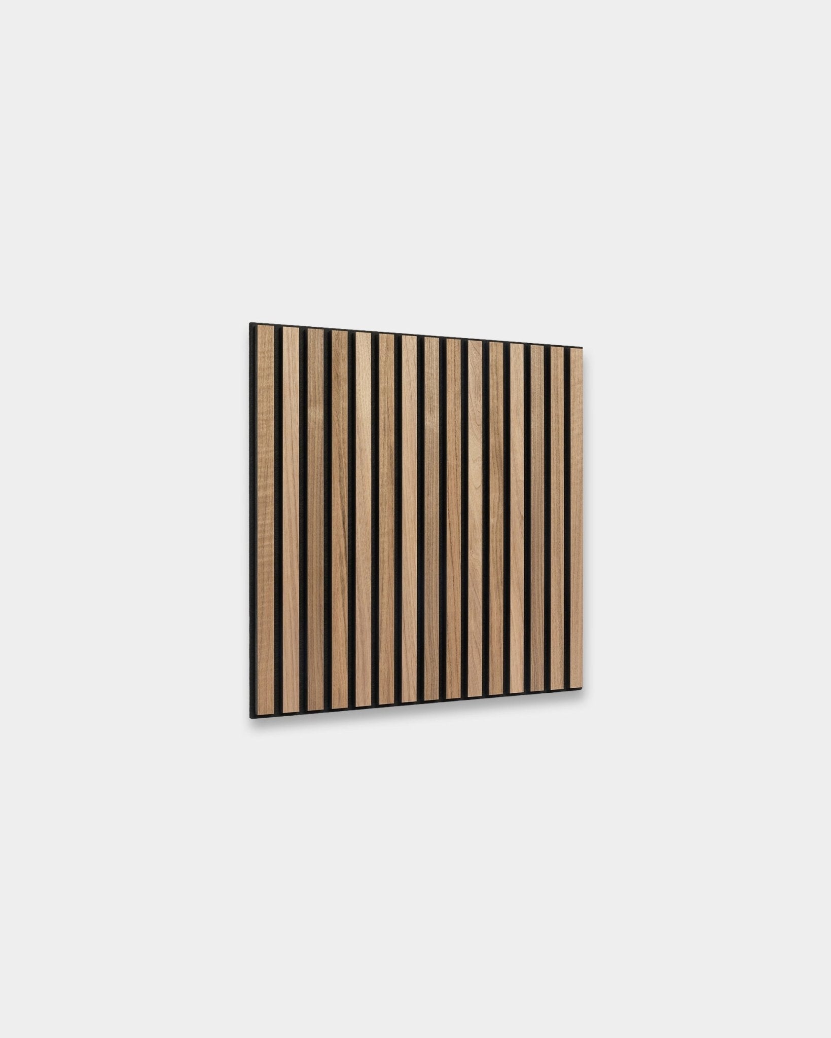 O WoodUpp Akupixel Painel acústico em nogueira, 60x60 cm, apresenta ripas de nogueira uniformemente espaçadas com intervalos de black, montadas numa parede cinzento-claro para um design escandinavo.