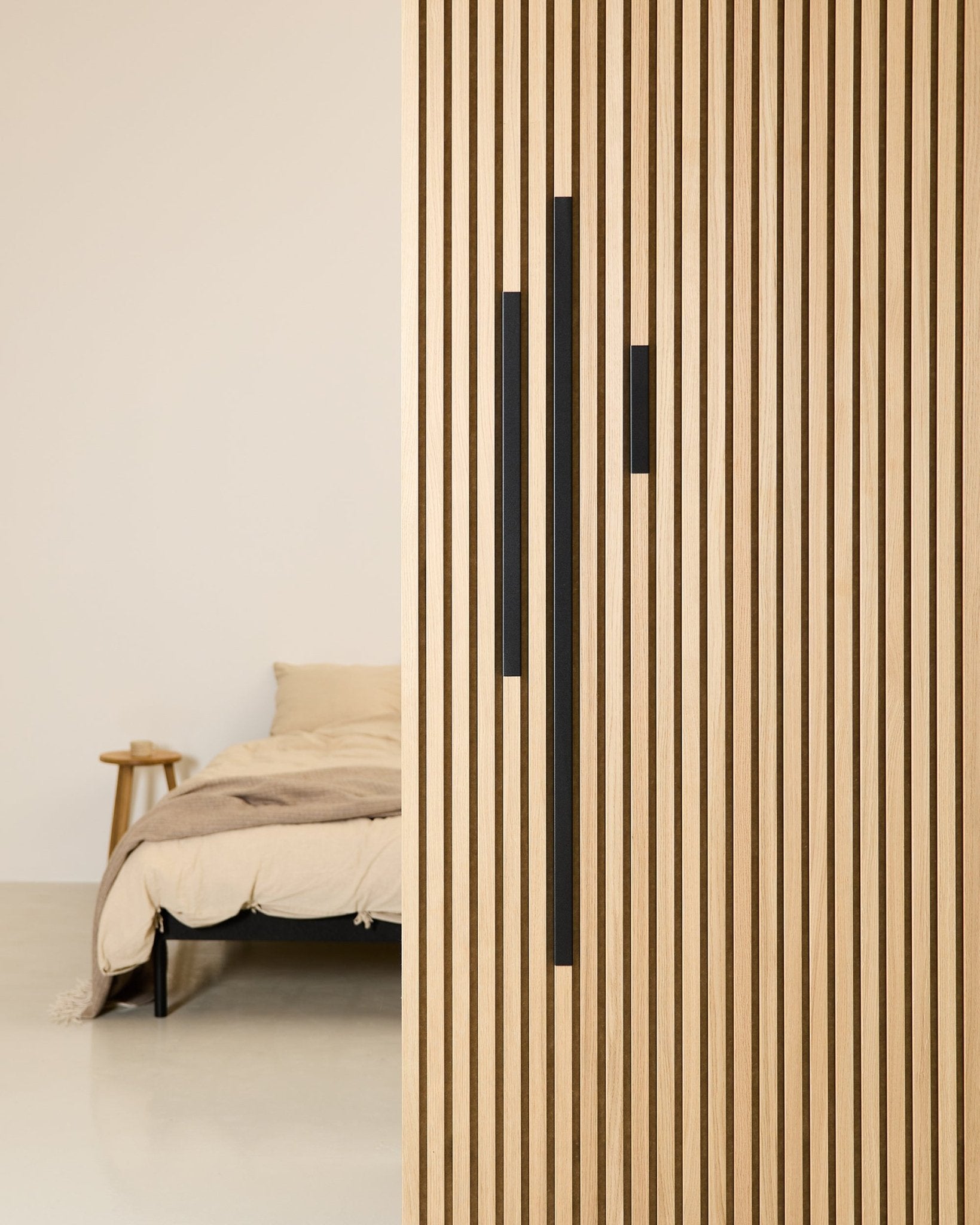 Quarto minimalista com uma cama beige e uma manta, parcialmente oculto por uma divisória WoodUpp Akupanel de 60 cm em alumínio Black, da série Liva Cover.