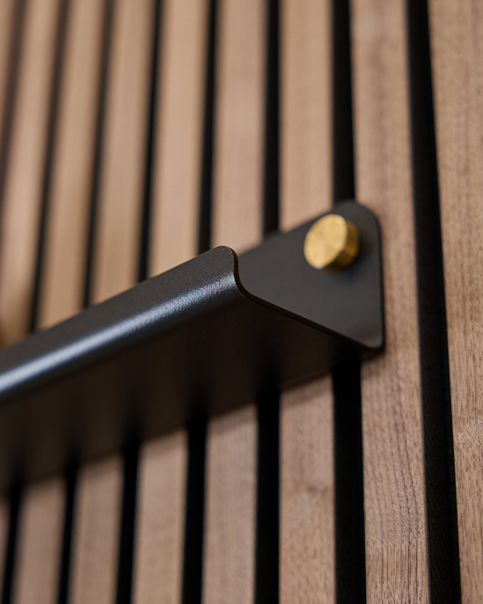 Close-up da Norr | Prateleira estreita (75,9 cm) da WoodUpp em black, com uma pega steel com parafusos dourados e superfície acústica com ranhuras verticais.