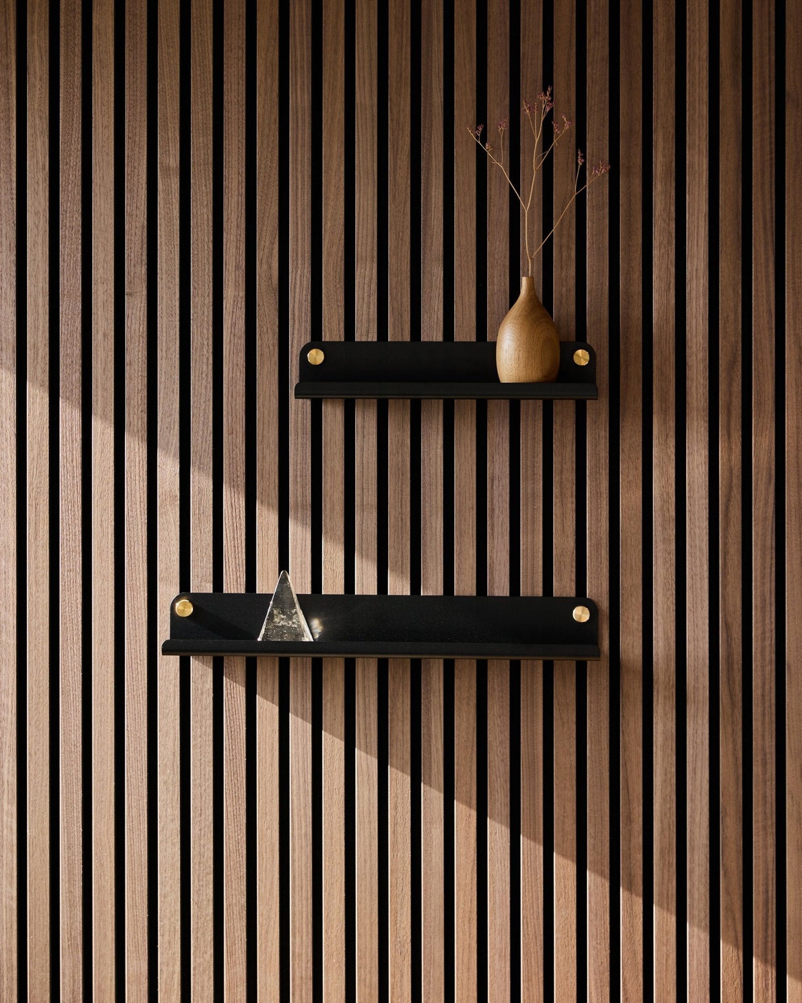 Duas prateleiras estreitas black WoodUpp Norr (35,9 cm) montadas num painel acústico ripado Nordic; a prateleira de cima com uma jarra com ramos secos, a de baixo com uma pirâmide de vidro.