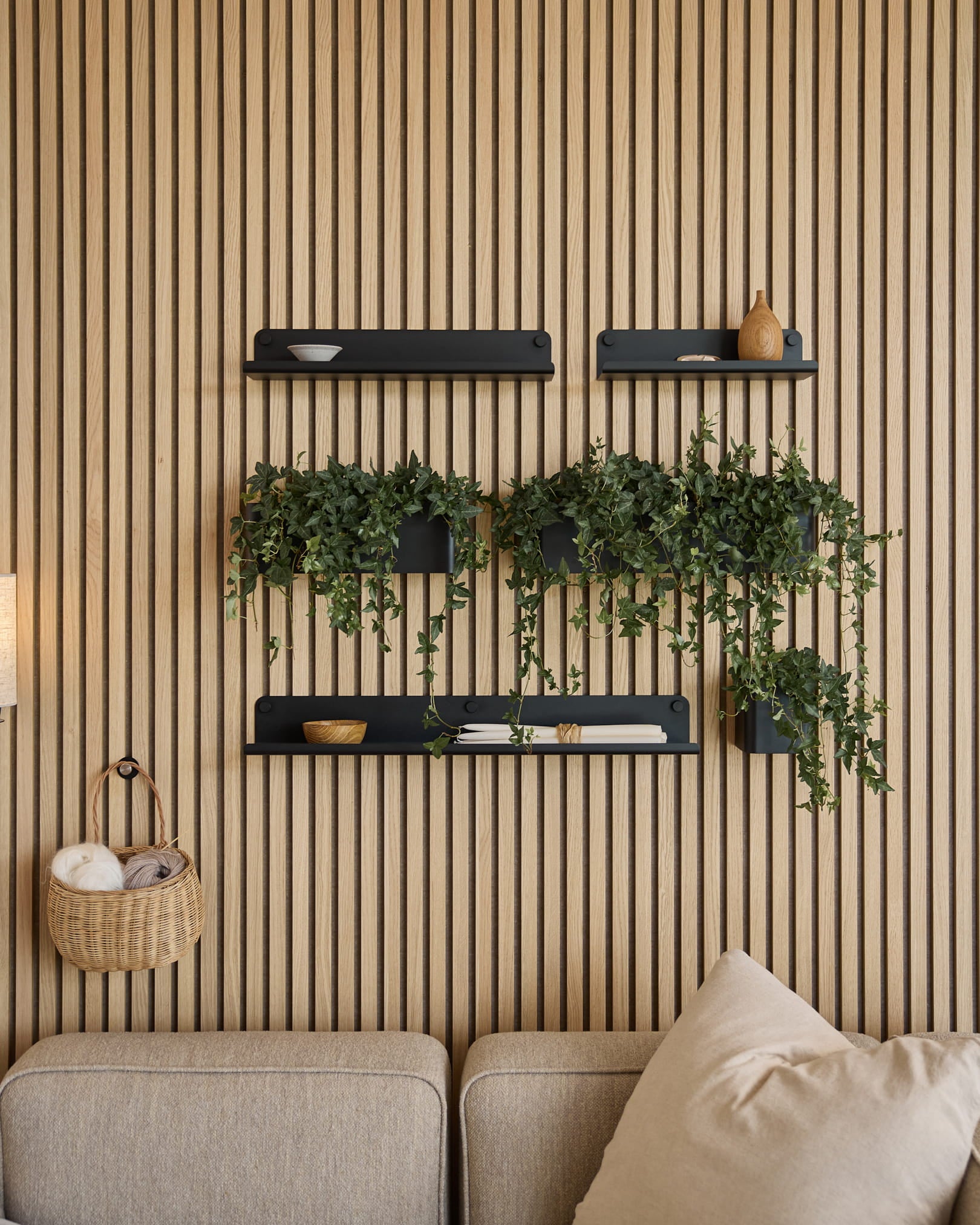 Sala de estar moderna com um painel acústico nórdico de ripas, prateleiras black, plantas pendentes na Plant Box Norr da WoodUpp (35,9 cm, Black) e um sofá beige.