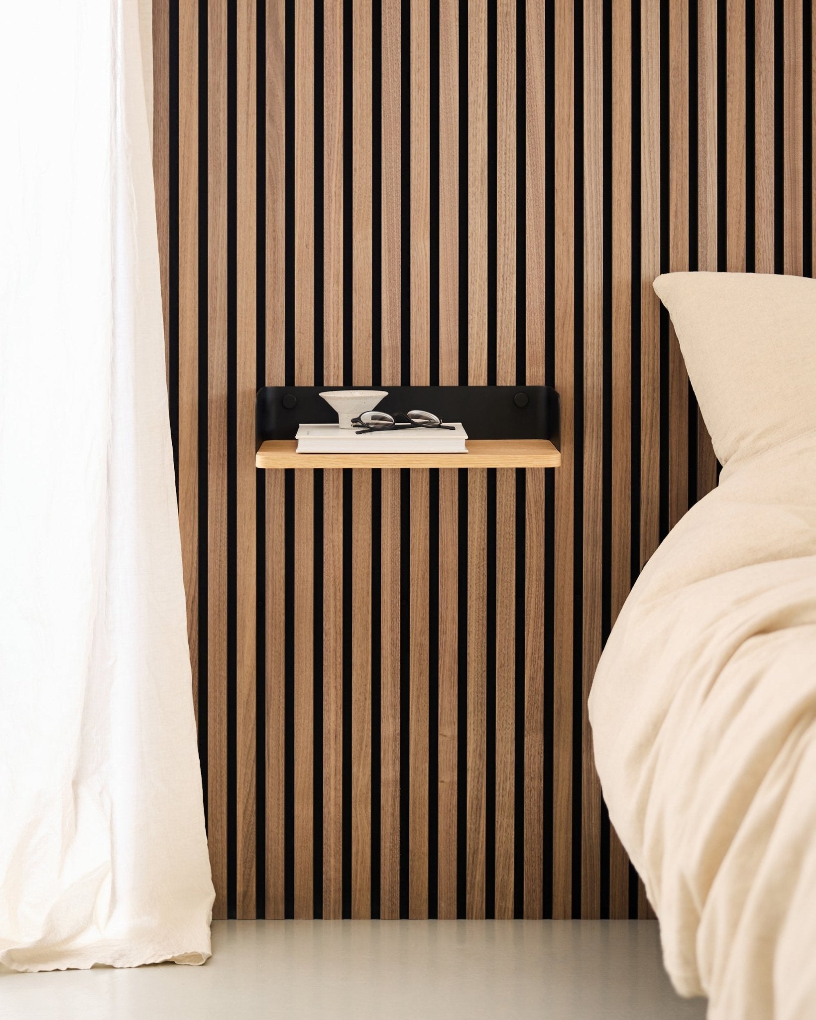Quarto minimalista com parede de ripas de madeira nórdica Painel acústico, estante WoodUpp Linn em Natural Oak e mesa de cabeceira suspensa ao lado de uma cama em beige.