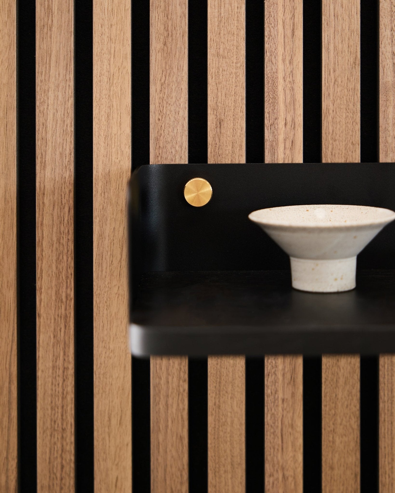 Taça de cerâmica colocada na prateleira Linn da WoodUpp, com 39,9 cm em black oak, com ripas vertical black e um apontamento em brass, refletindo o design minimalista nórdico.