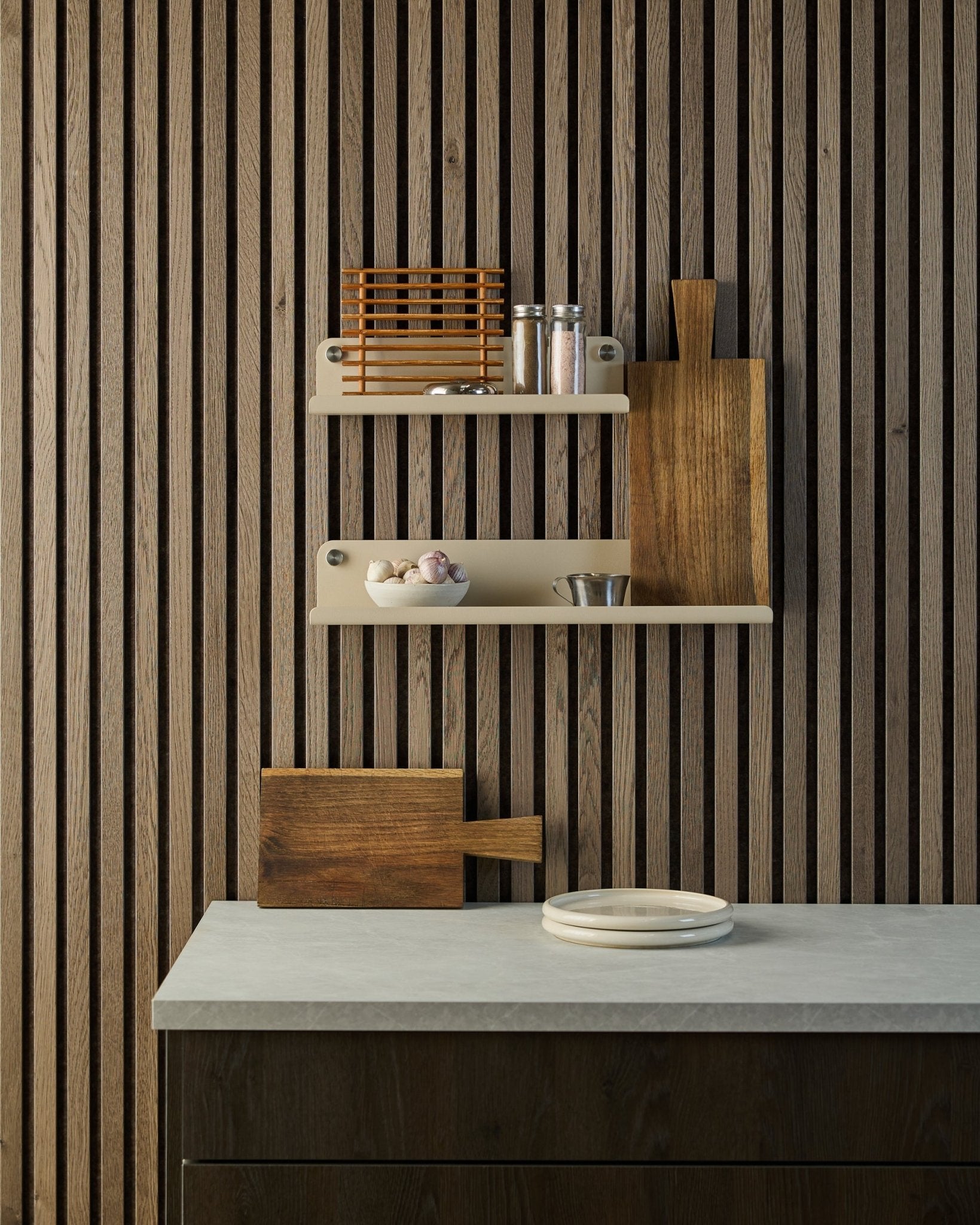 Cozinha minimalista com parede acústica de ripas de madeira nórdica Akupanel, prateleiras abertas com especiarias e taças, bancada com pratos brancos e uma tábua de cortar.