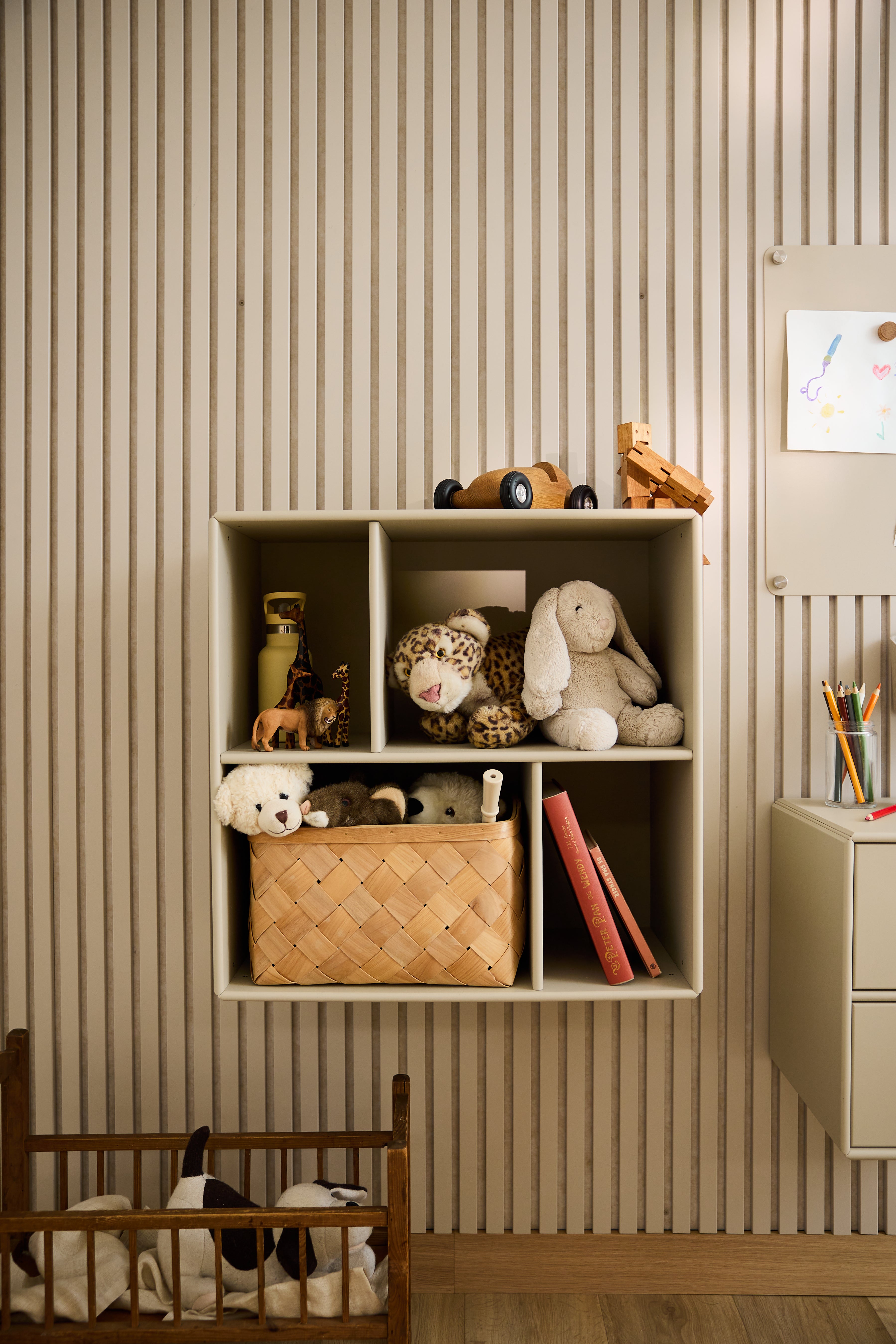 O armário aberto WoodUpp Arka, em bege, com brinquedos e livros, em contraste com o papel de parede às riscas num quarto de criança, destaca o design nórdico minimalista.