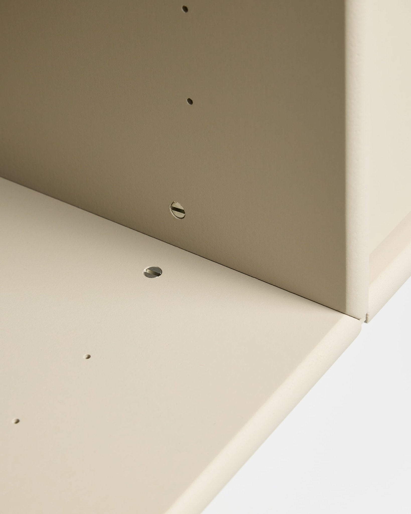 Grande plano de duas placas bege da consola de televisão «Arka» da WoodUpp, unidas em ângulo reto com orifícios pré-perfurados para montagem modular e organização de cabos.