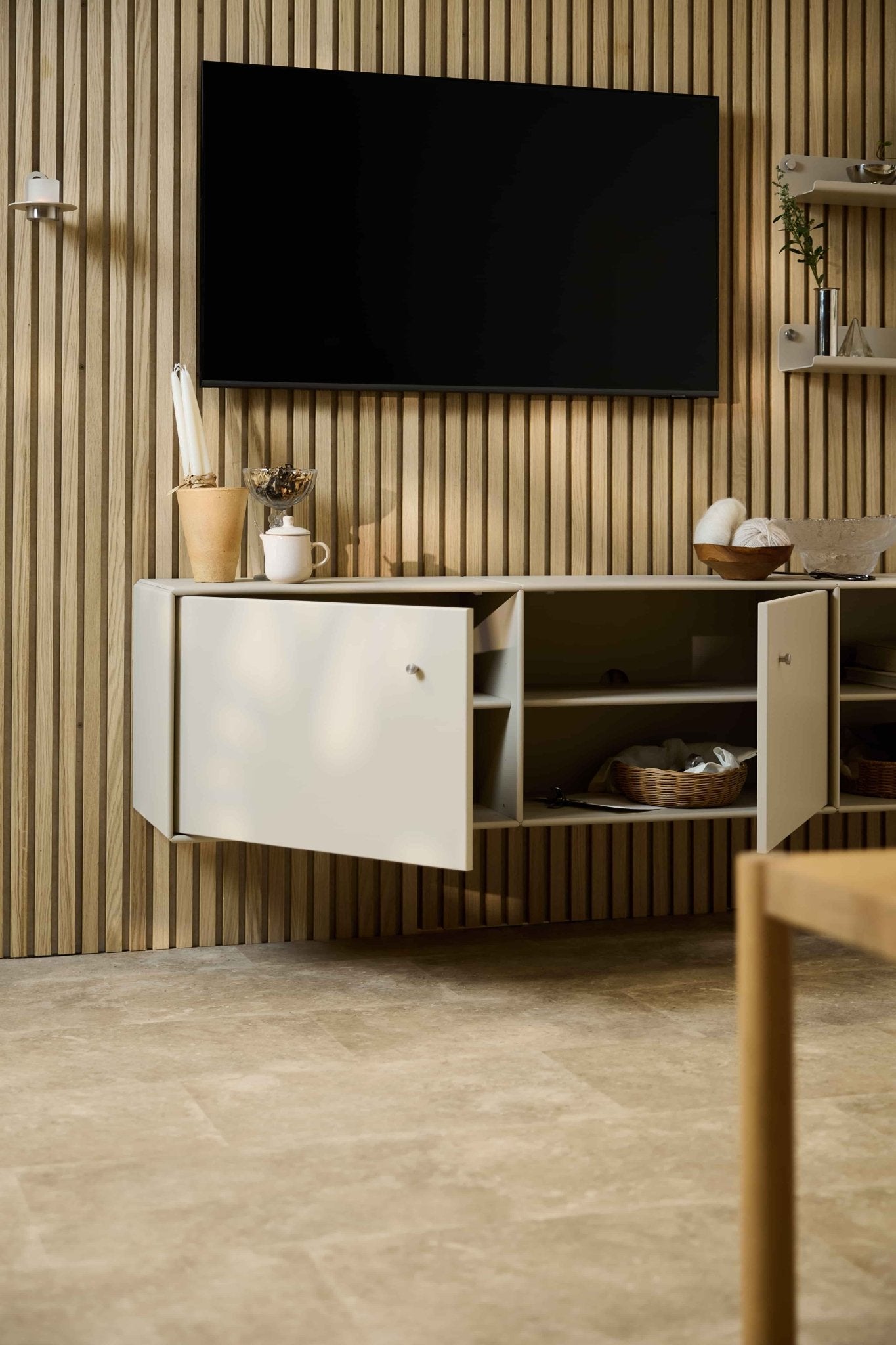 Sala de estar moderna com a consola de televisão Arka em bege da WoodUpp, situada por baixo de um armário e de um televisor, numa parede acústica com ripas de madeira Akupanel de estilo nórdico. Mobiliário modular.
