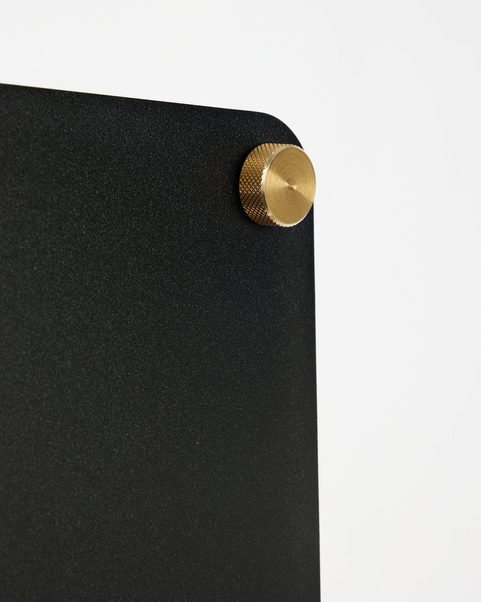 Grande plano do quadro magnético acústico WoodUpp Norr black (small), com um canto arredondado e fixação com parafuso dourado, sobre fundo branco.