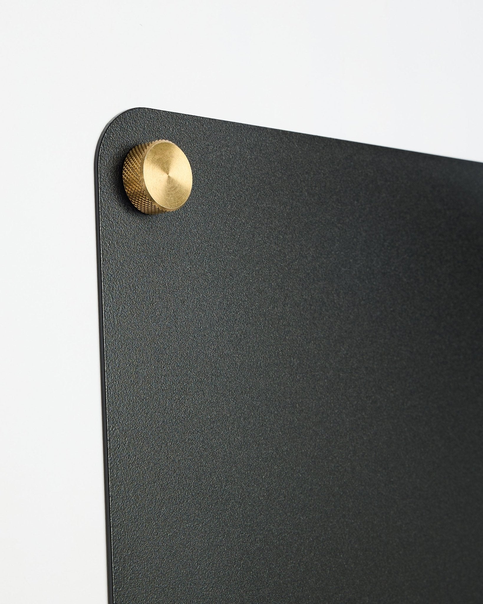 Grande plano de um large black Norr Quadro Magnético da WoodUpp, parte da coleção CREATE, com uma fixação metálica redonda dourada-colored no canto superior.