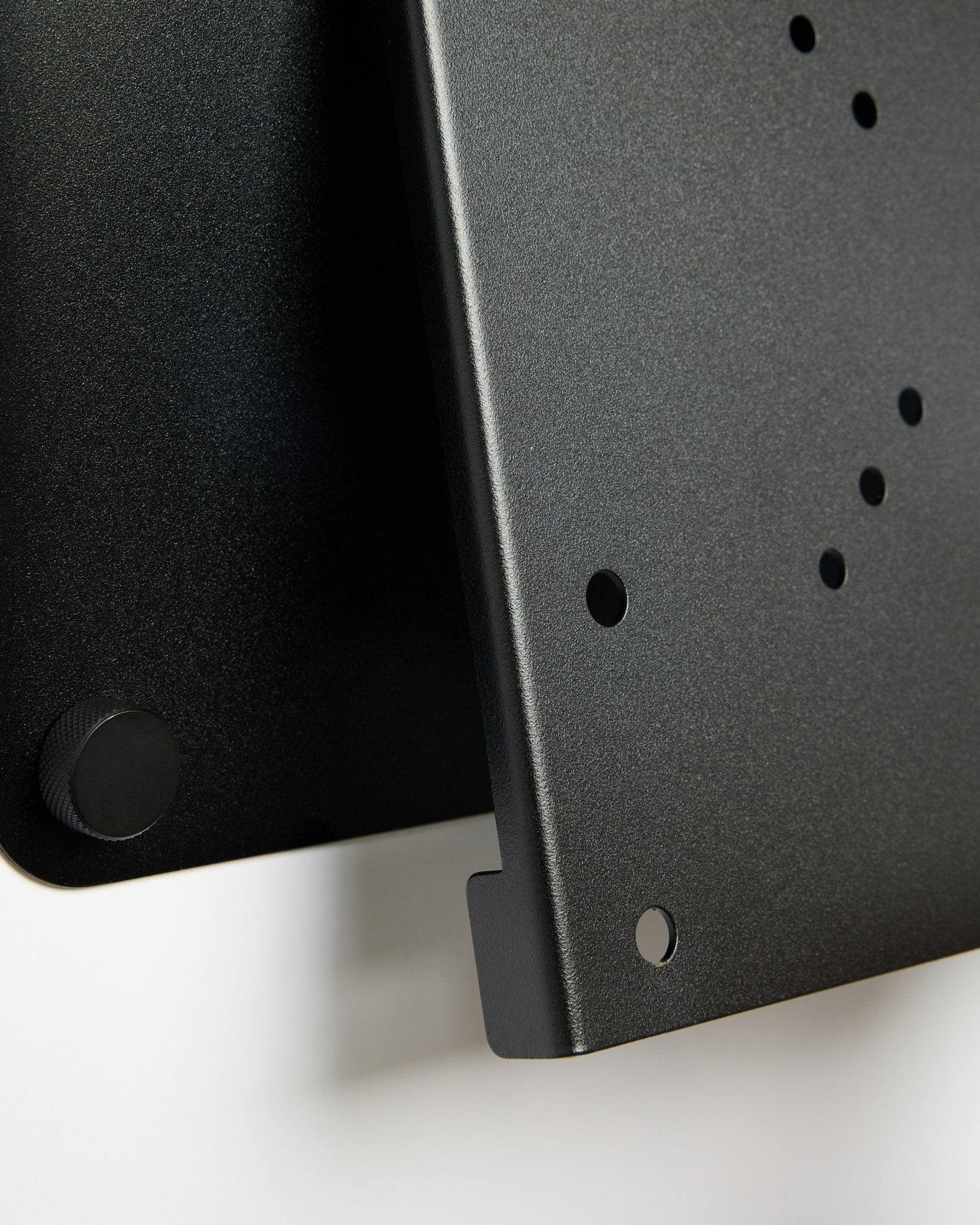 Plano aproximado do suporte de TV Fjell (small) da WoodUpp, um suporte metálico black com furos circulares e botão de ajuste, apresentado sobre um fundo branco.