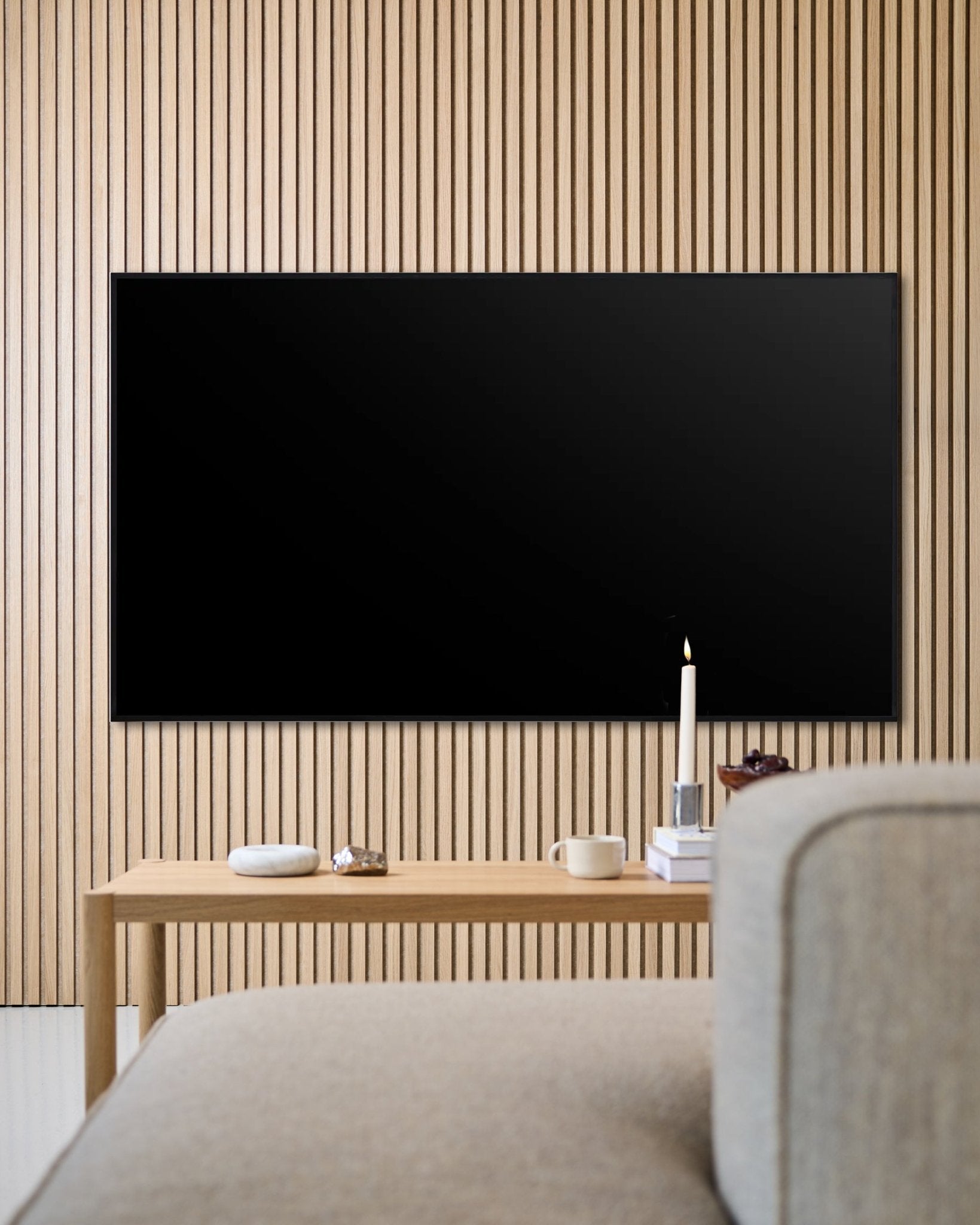 Sala de estar moderna com TV de ecrã plano montada na parede, parede ripada acústica em madeira Akupanel e mesa de centro em madeira para um ambiente acolhedor.