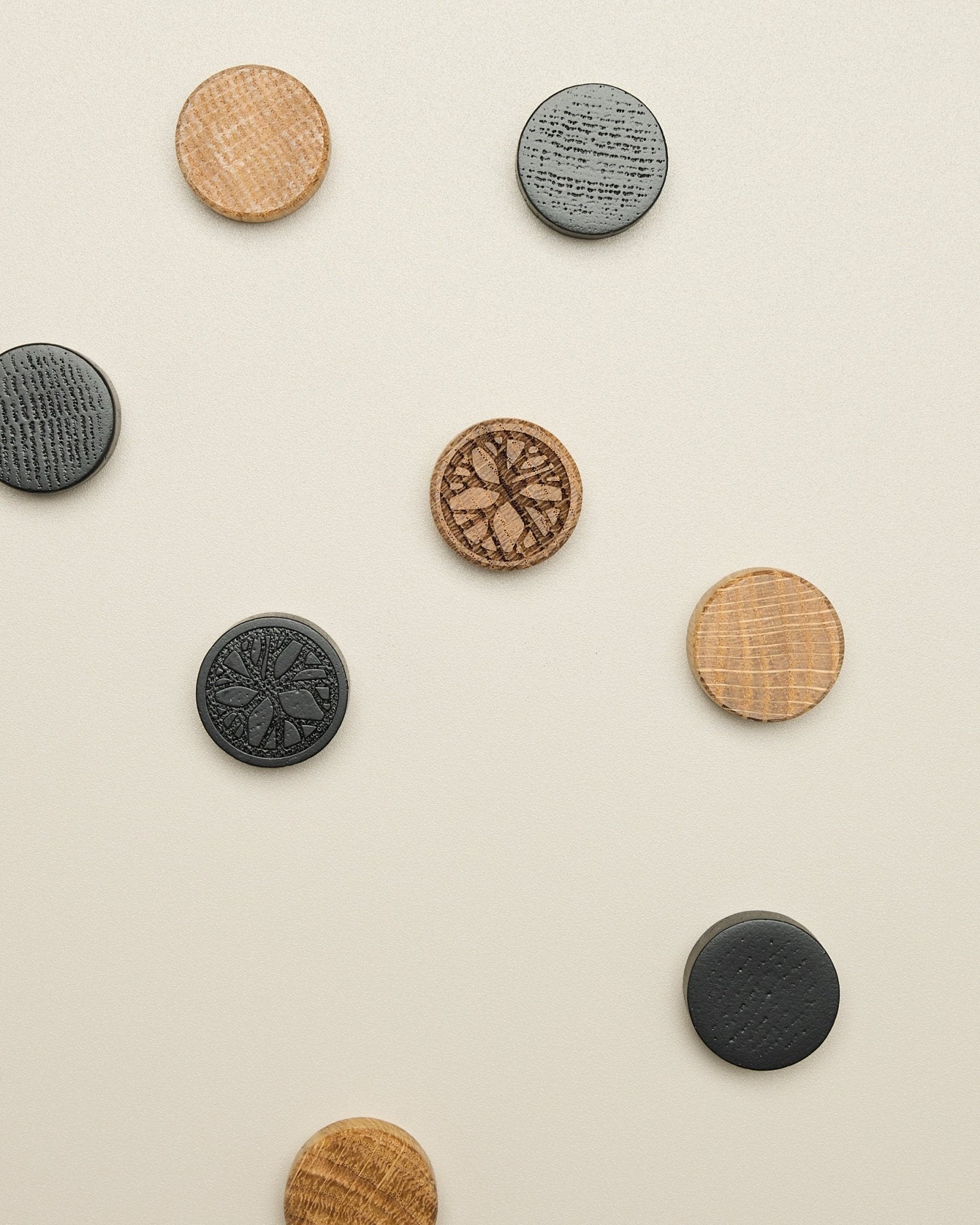O conjunto de ímanes Norr da WoodUpp inclui quatro discos com padrão natural oak e black, cuidadosamente colocados sobre uma superfície clara em beige; acessório para Akupanel.