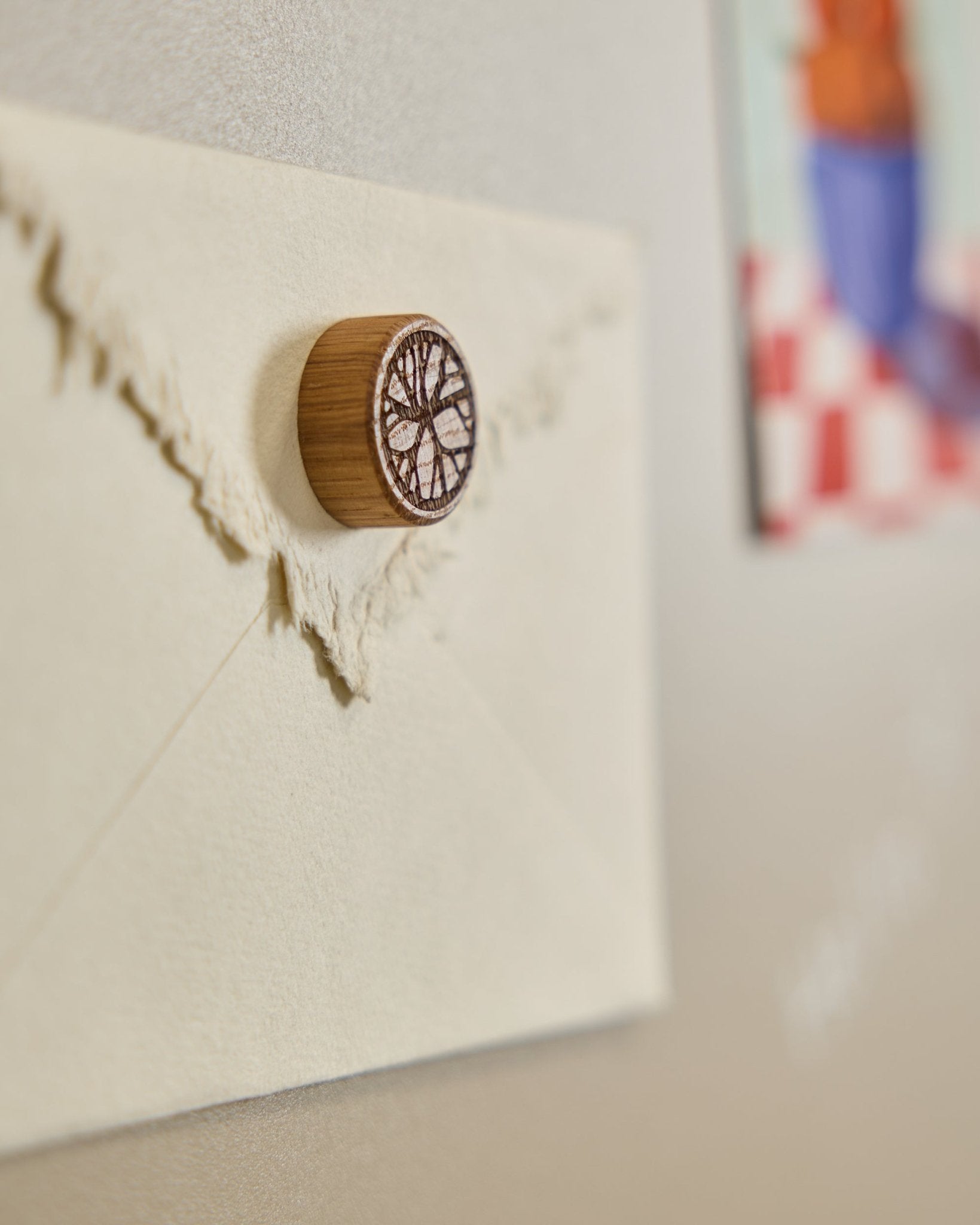 Um envelope em tom creme está preso a um Painel acústico com um íman Norr Natural Oak da WoodUpp, com um desenho minimalista de árvore.