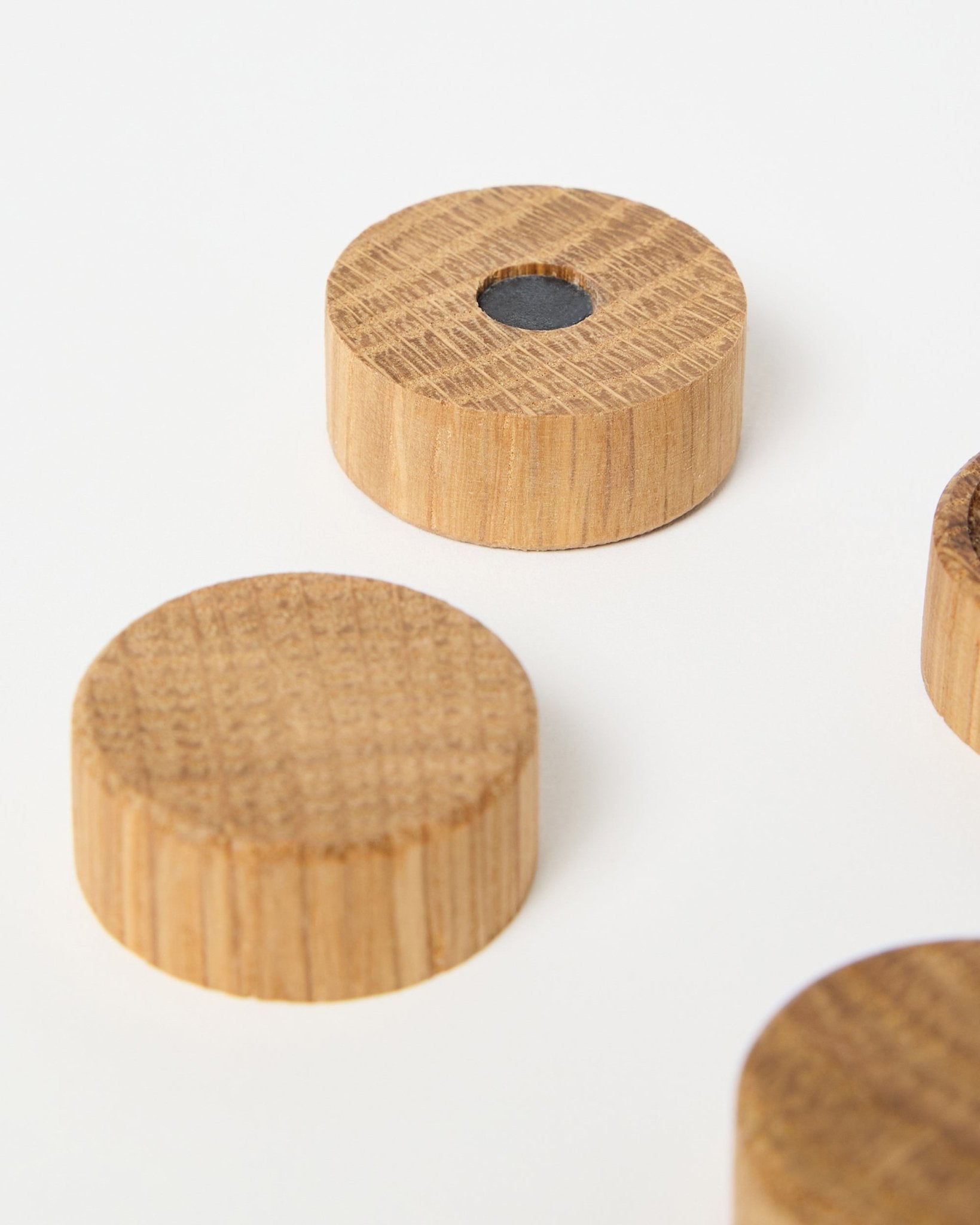 Conjunto de quatro ímanes natural oak da WoodUpp, concebidos para usar com painéis acústicos de madeira Akupanel, um deles com um íman de neodímio central para maior fixação, apresentados sobre fundo branco.