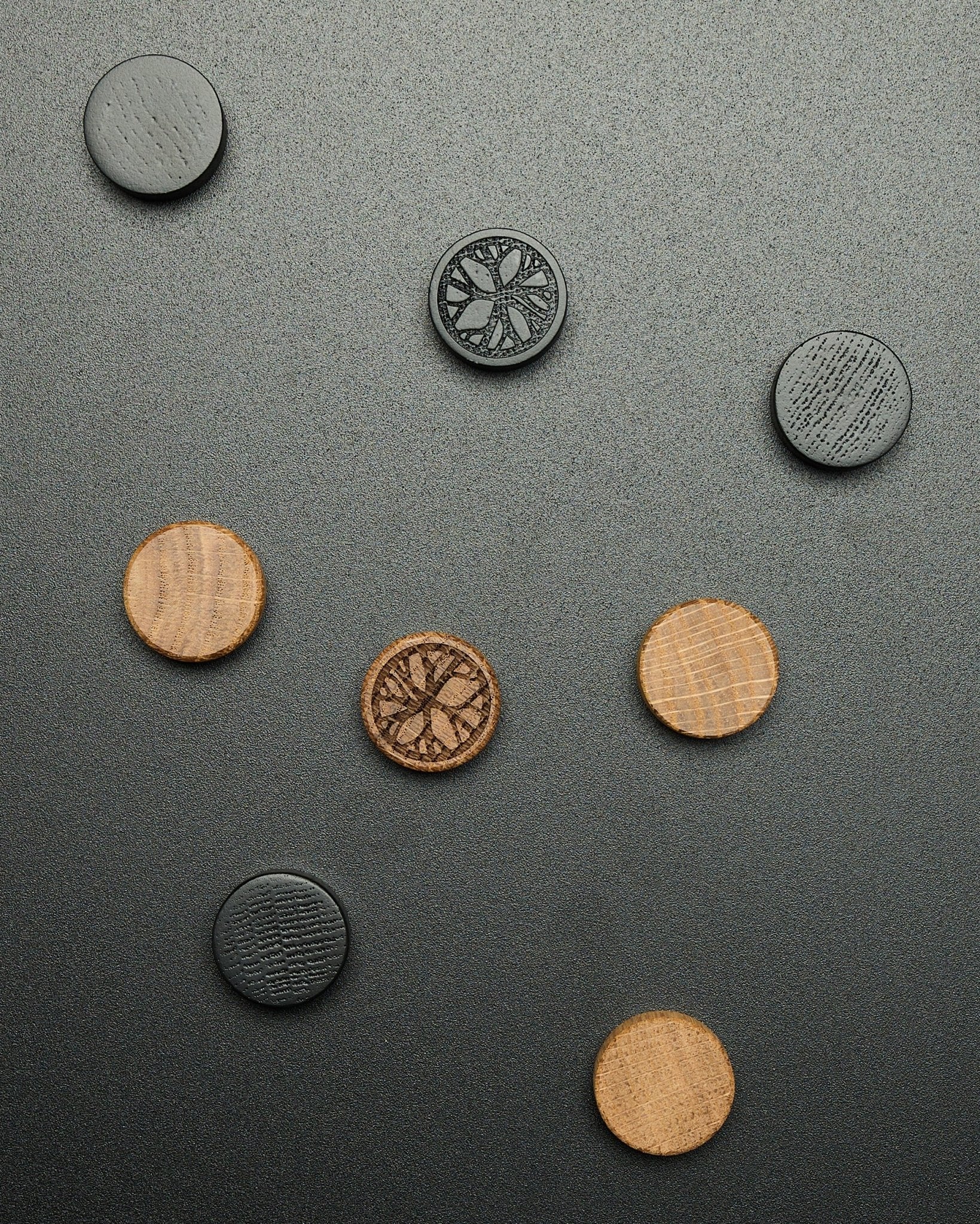 Quatro ímanes redondos black oak do conjunto de ímanes Norr da WoodUpp, dispostos de forma solta sobre uma superfície escura texturada, concebidos como acessórios Akupanel.