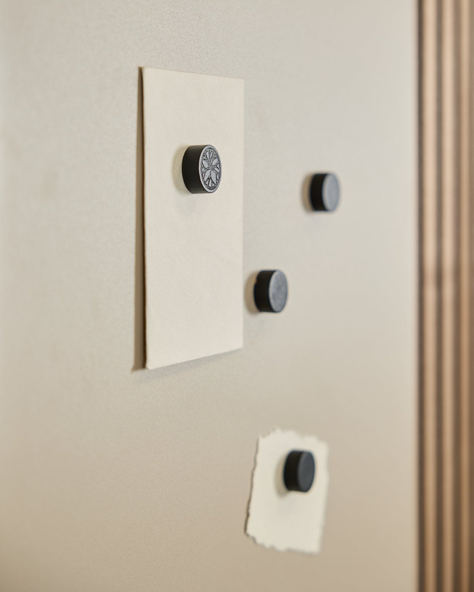 Quatro ímanes do conjunto Norr da WoodUpp em Black Oak (4 unid.) seguram duas folhas de papel num quadro magnético Norr, com parte de um(a) Painel acústico visível à direita.