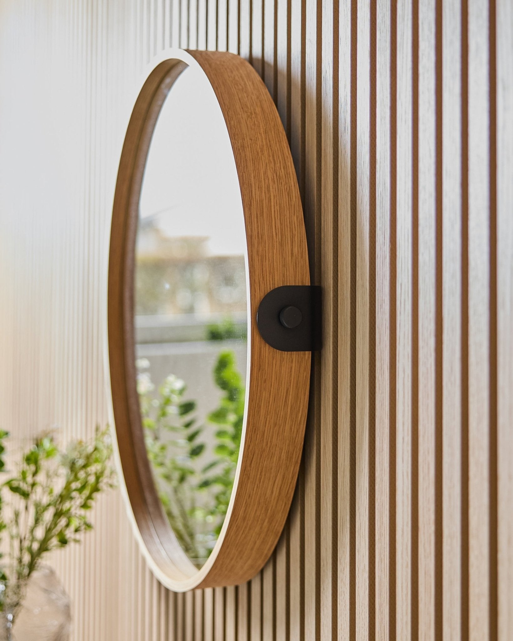 Linn | Mirror / Natural Oak da WoodUpp montado numa parede Painel acústico às riscas, a refletir vegetação e luz natural de uma janela próxima.