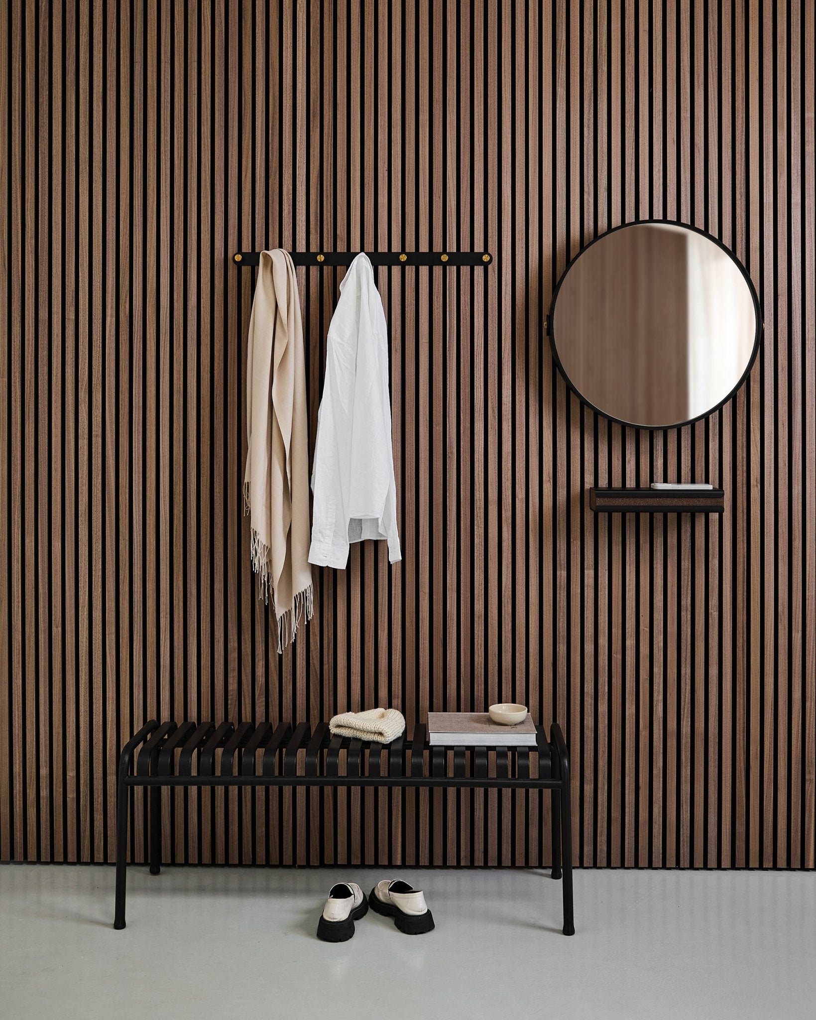 Hall de entrada minimalista com um WoodUpp Linn | Mirror em Black Oak, painel acústico nórdico de ripas, banco, prateleira, casaco e cachecol pendurados, e sapatos no chão.