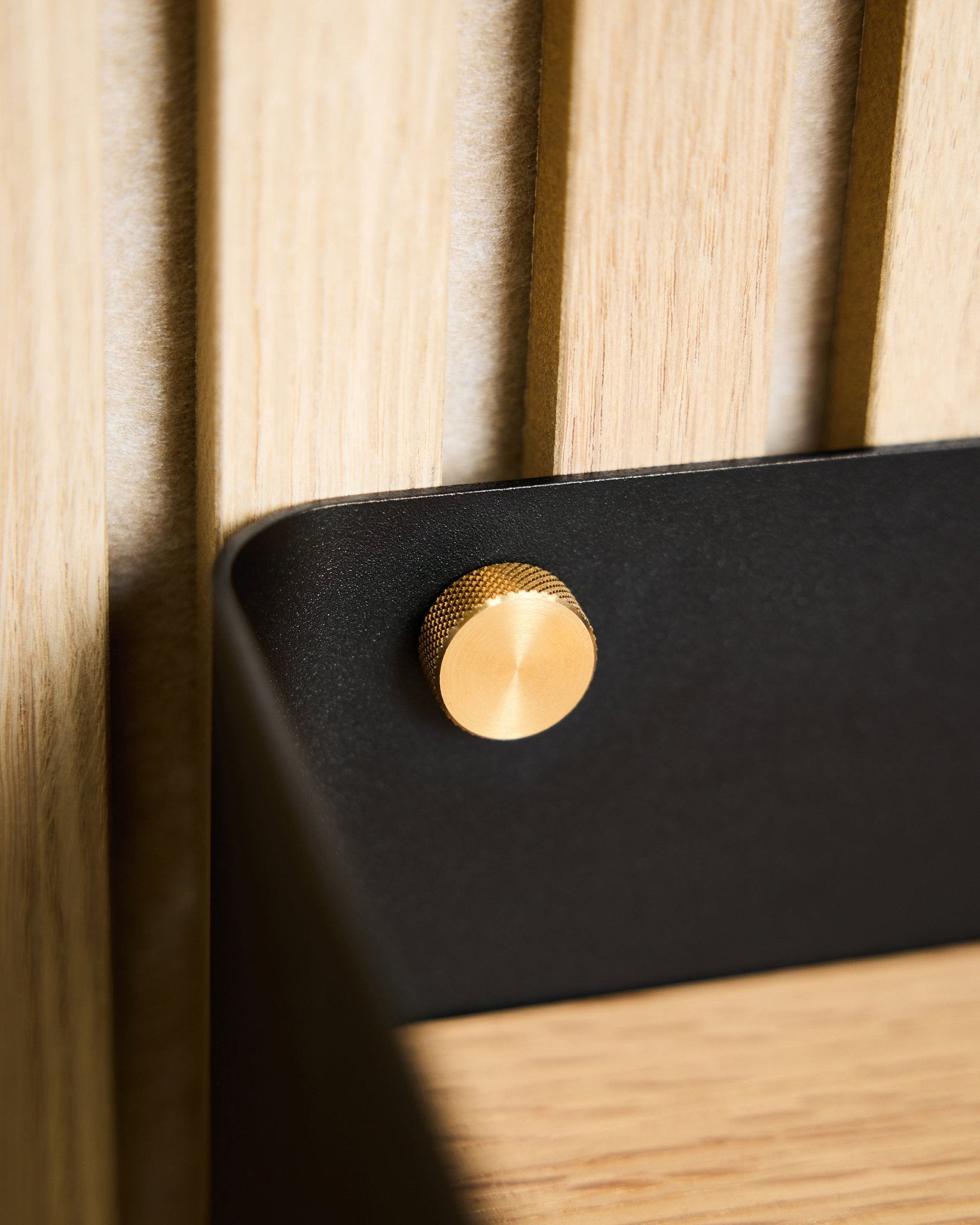 Grande plano de dois parafusos de aperto manual WoodUpp brass (M5x10 mm, 20x8.8), fixados a um suporte black montado numa superfície Painel acústico de madeira nórdica clara.