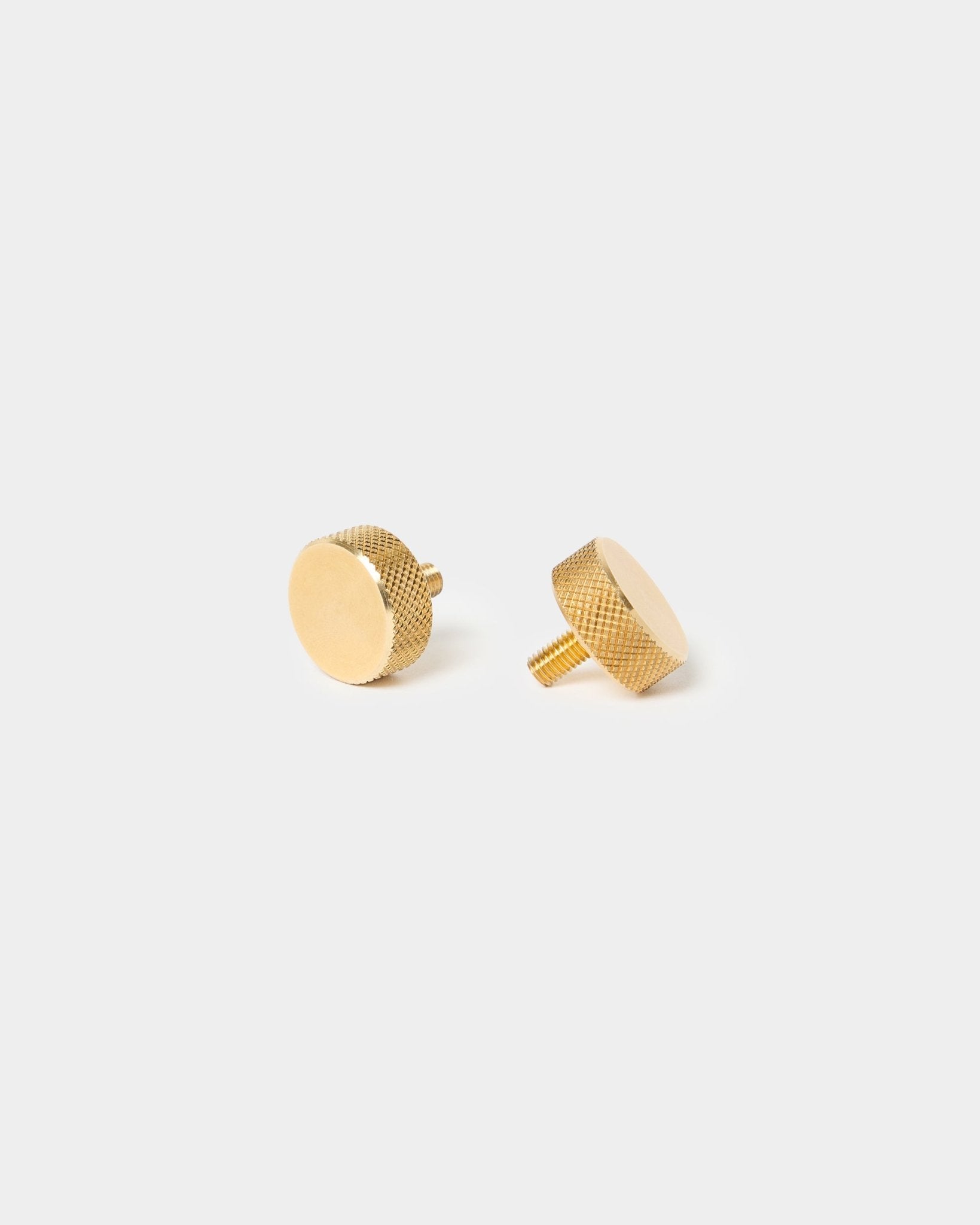 Par de parafusos de aperto manual WoodUpp brass (M5x10 mm, 20x8.8), com rebordos texturados e hastes curtas, concebidos para acessórios Akupanel, sobre um fundo liso e claro.