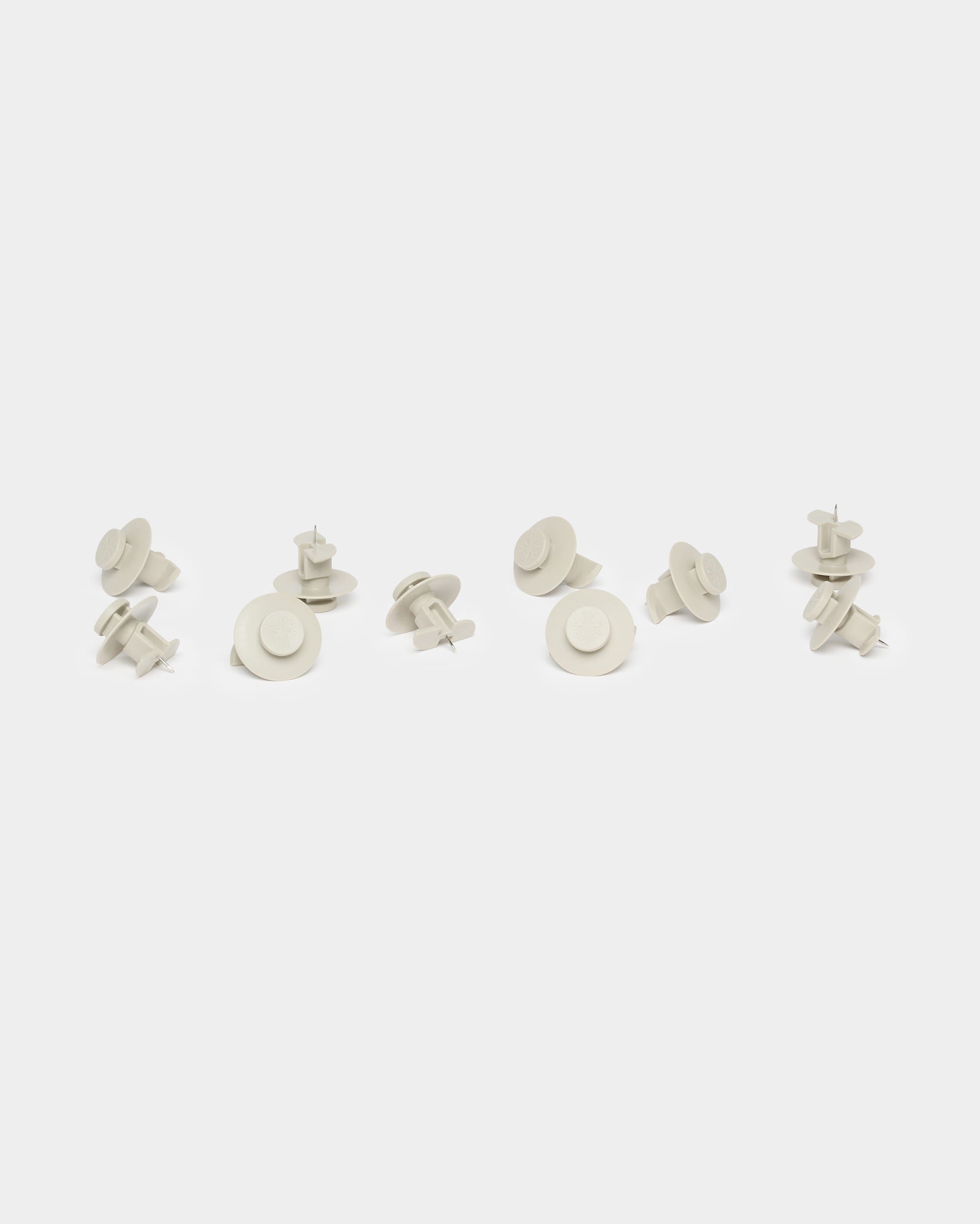 Dez alfinetes Dupps bege da WoodUpp, utilizados como acessórios do Akupanel, estão agrupados de forma espalhada sobre um fundo branco liso.