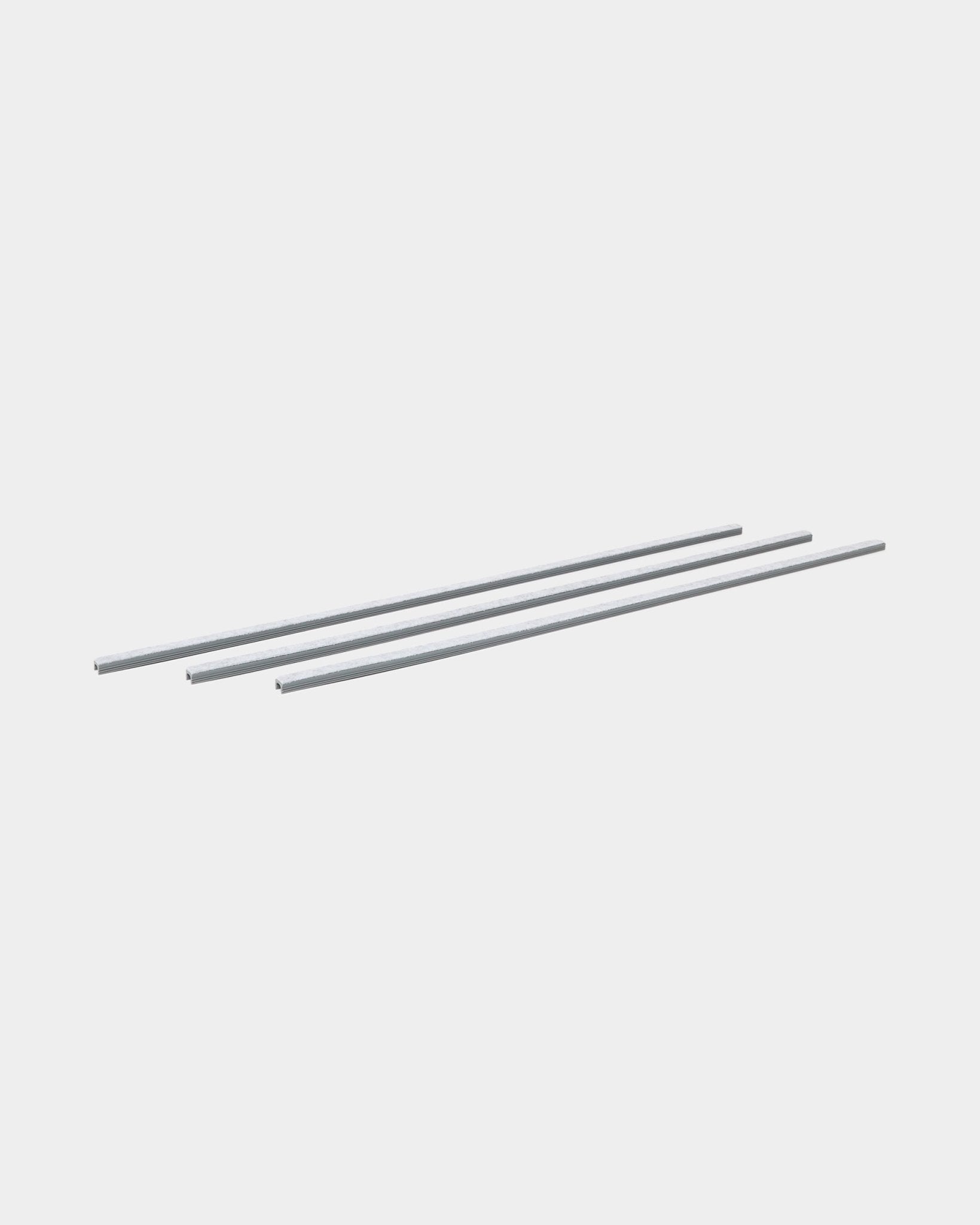 Três grey Dupps Pop-on Cable Covers (3 unid.) da WoodUpp estão alinhadas em paralelo, concebidas para organizar cabos com painéis acústicos de madeira Akupanel.