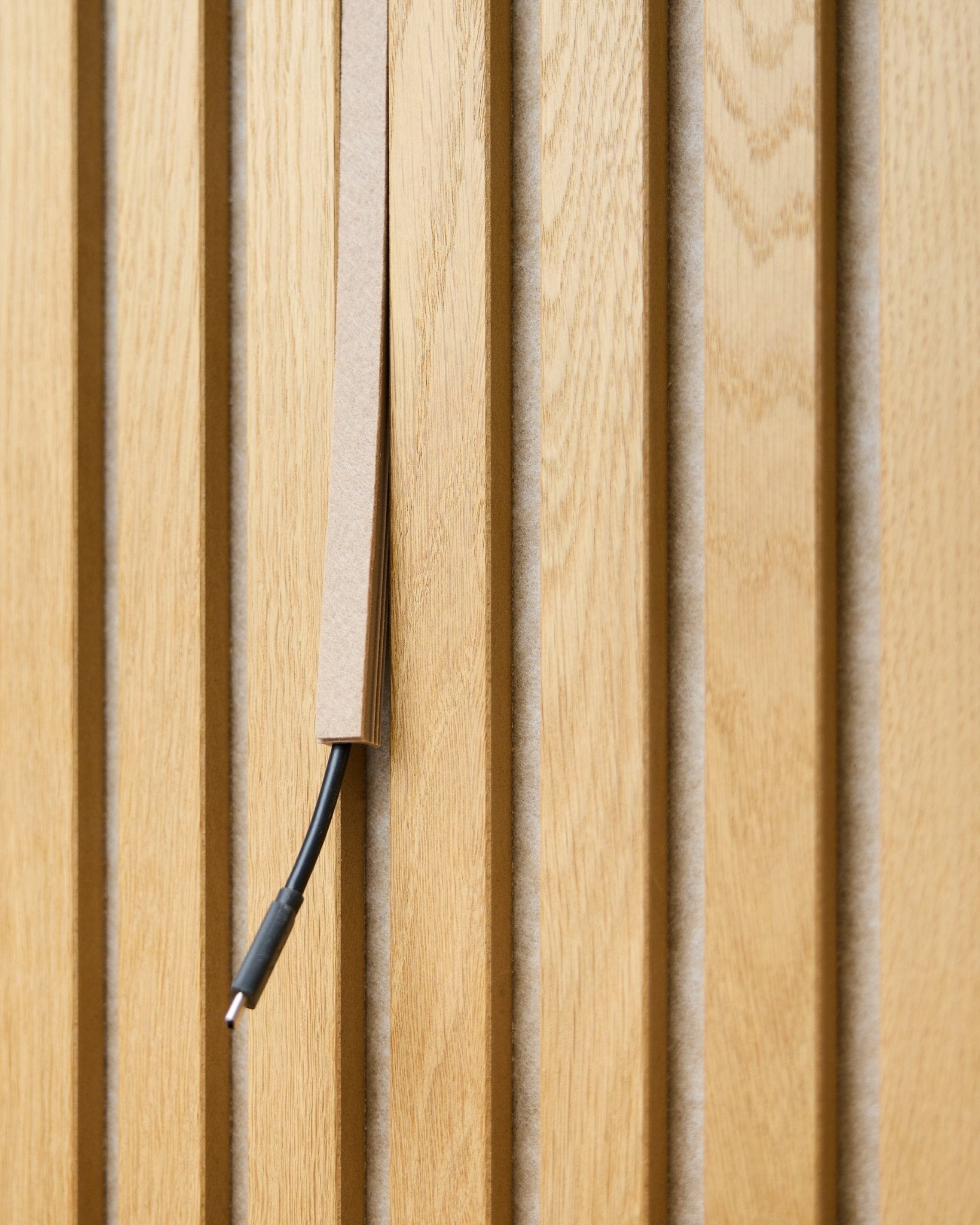 Um cabo black com gestão de cabos fica parcialmente oculto numa Dupps Beige Pop-on Cable Cover da WoodUpp, montada em ripas acústicas de madeira vertical Akupanel.