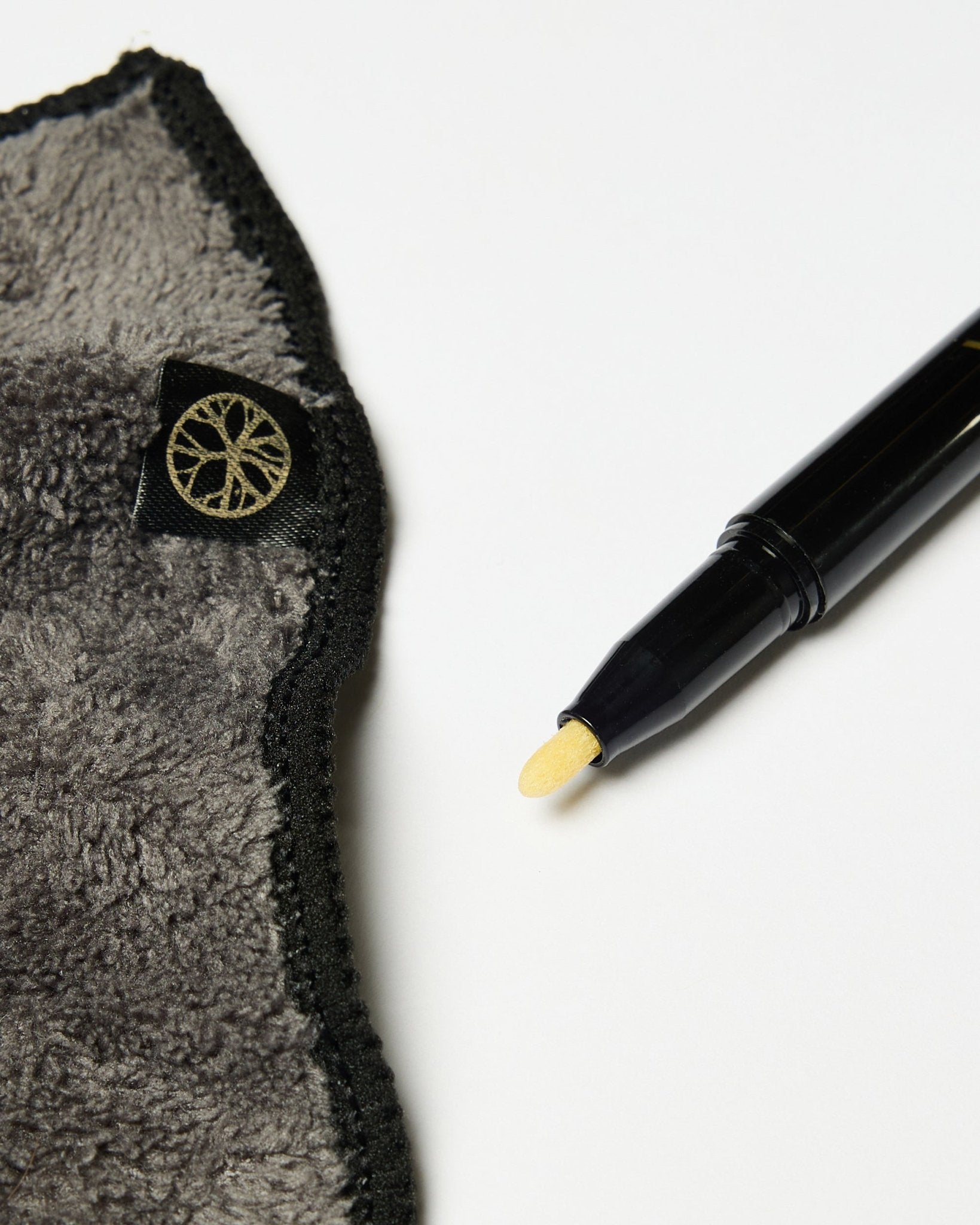 O conjunto Blackboard Norr da WoodUpp inclui um marcador de tinta de giz black com ponta amarela e um pano de microfibra cinzento com etiqueta dourada, apresentados sobre uma superfície branca.
