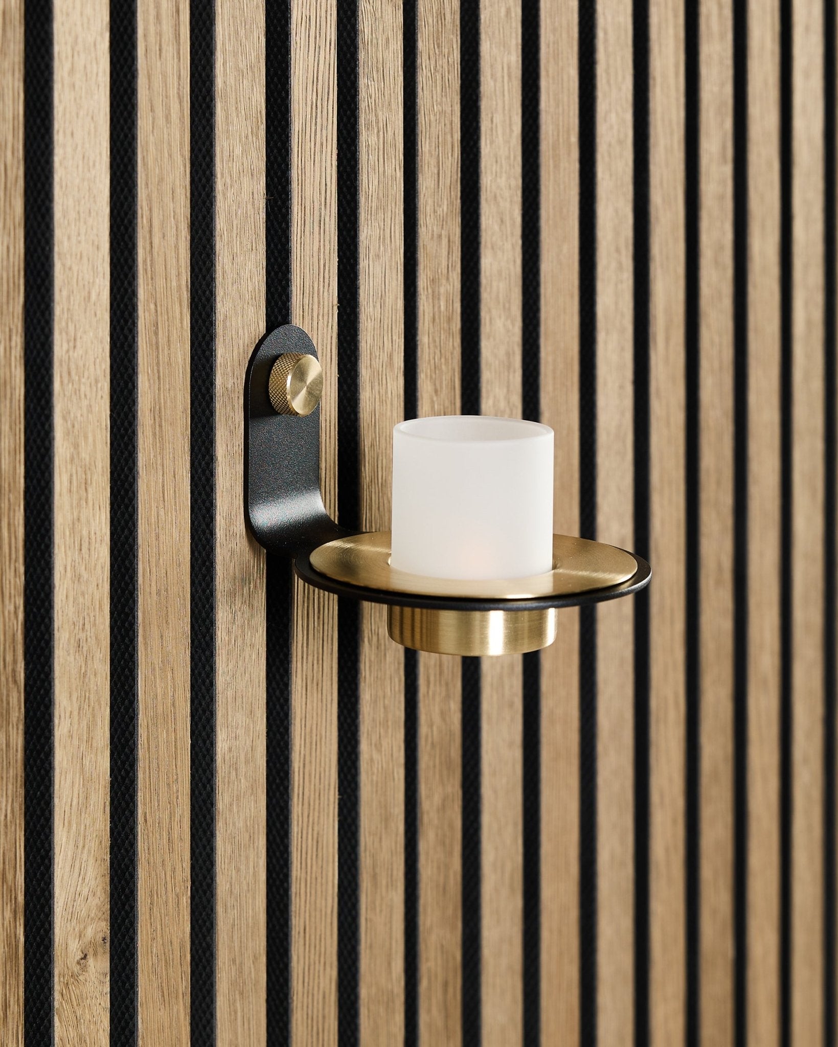 O Suporte para Velas Norr em black e brass da WoodUpp está montado num painel acústico de madeira nórdico Akupanel, com ripas black vertical.