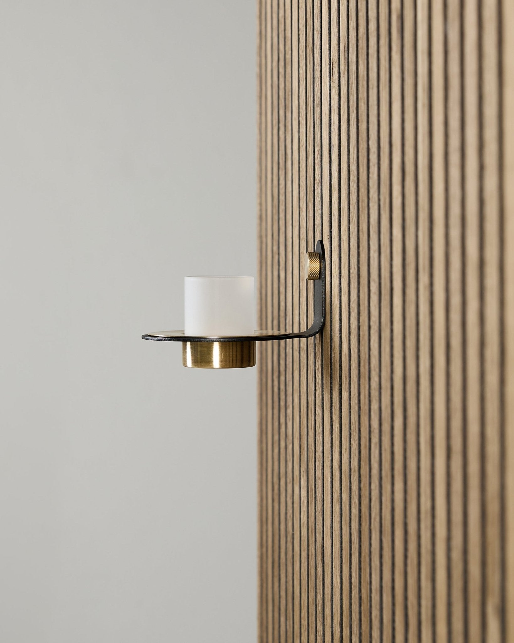 Suporte para Velas Norr em black e brass da WoodUpp, montado num vertical Akupanel Painel acústico, com vidro fosco e detalhes em brass.