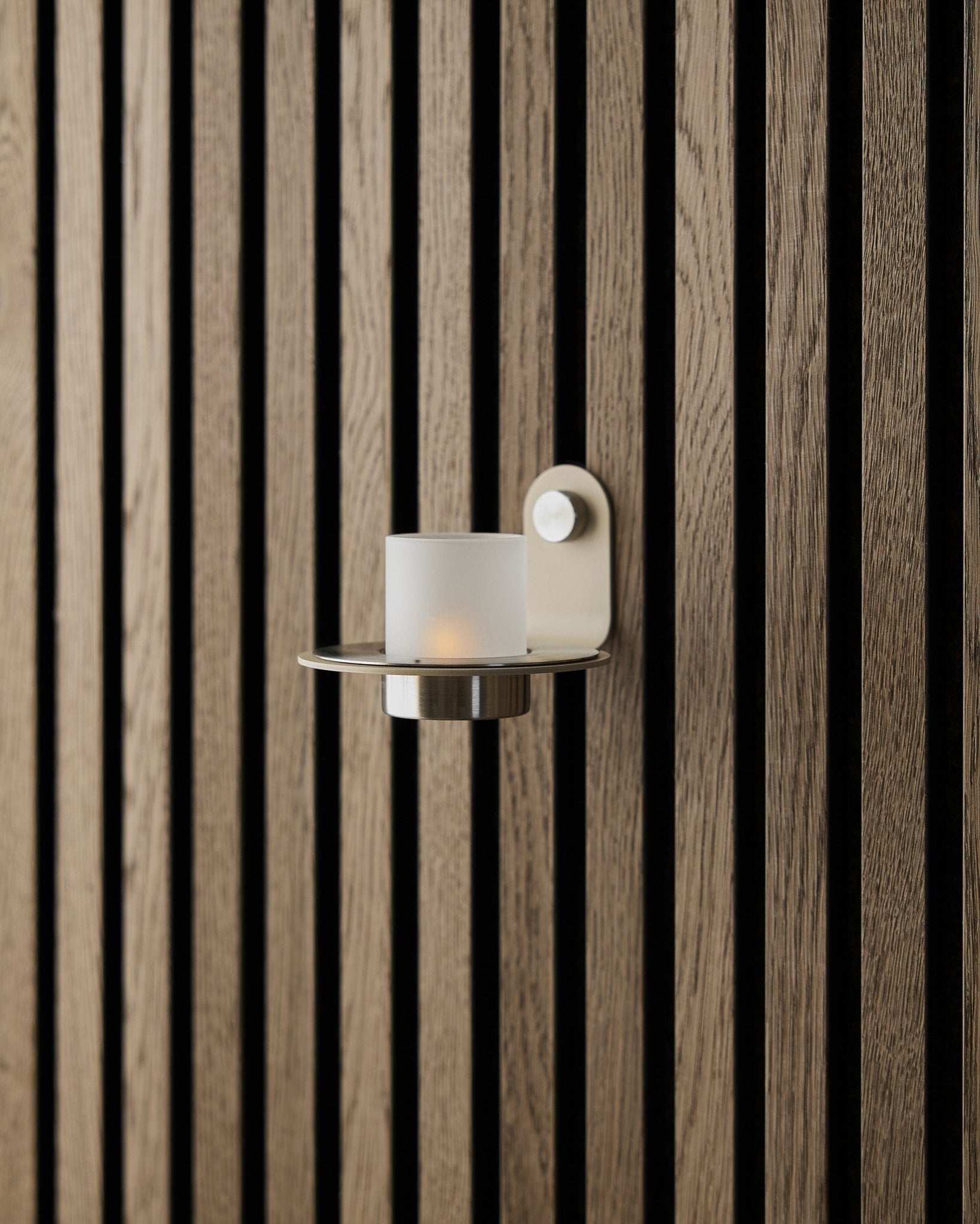 O suporte para velas Norr em aço inoxidável steel beige da WoodUpp, apresentado numa parede com Painel acústico Akupanel beige.
