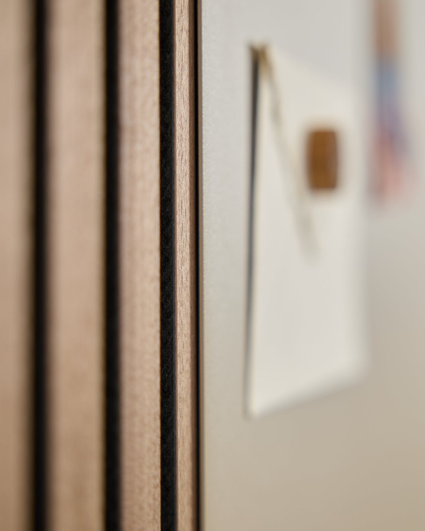 Grande plano de um painel acústico de madeira Akupanel da WoodUpp com ripas vertical, ao lado de um Quadro Magnético large beige Norr desfocado em segundo plano.