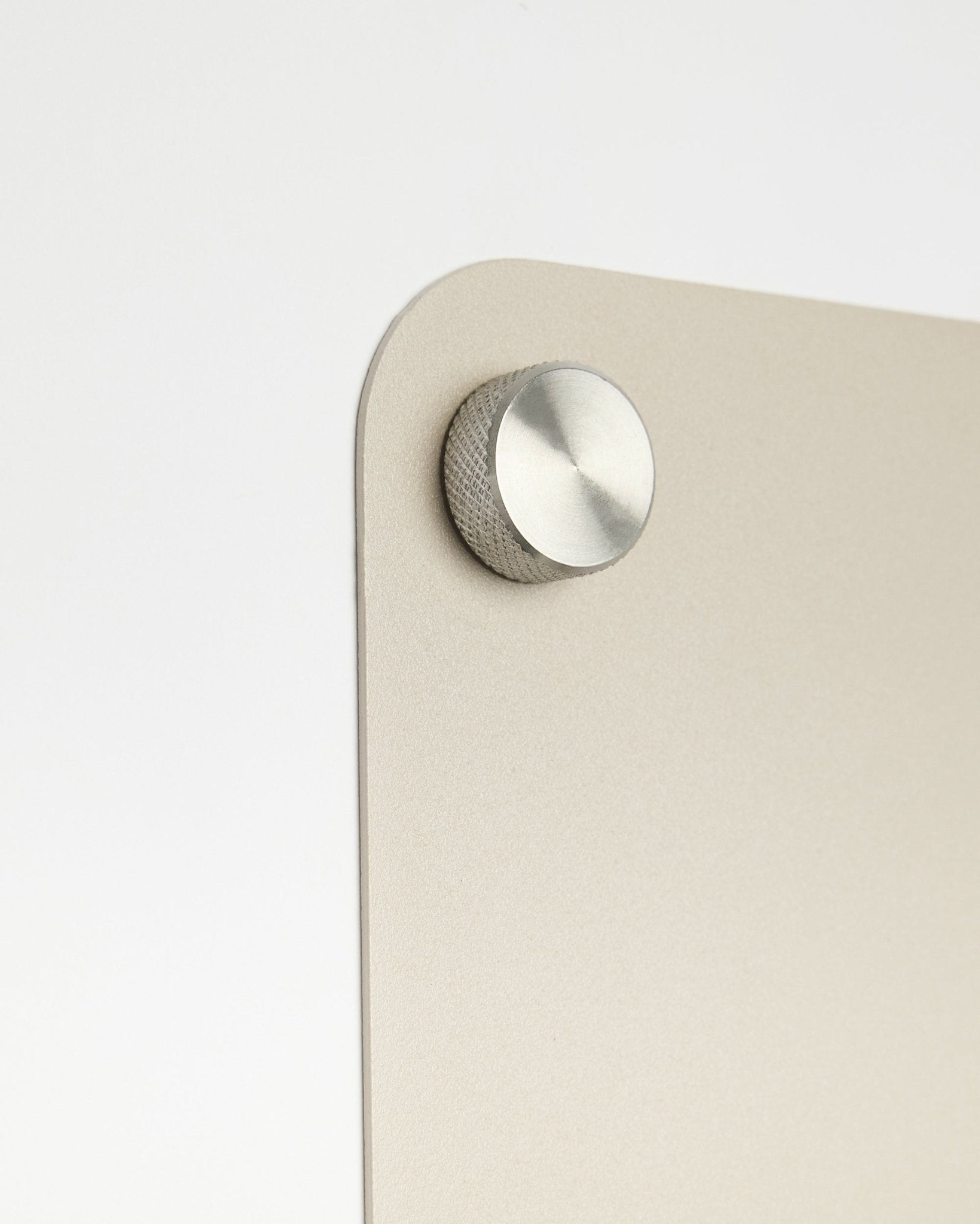 Grande plano de um acessório com botão redondo em metal fixado ao Quadro Magnético large beige Norr da WoodUpp, com detalhe em vidro fosco sobre um fundo branco.