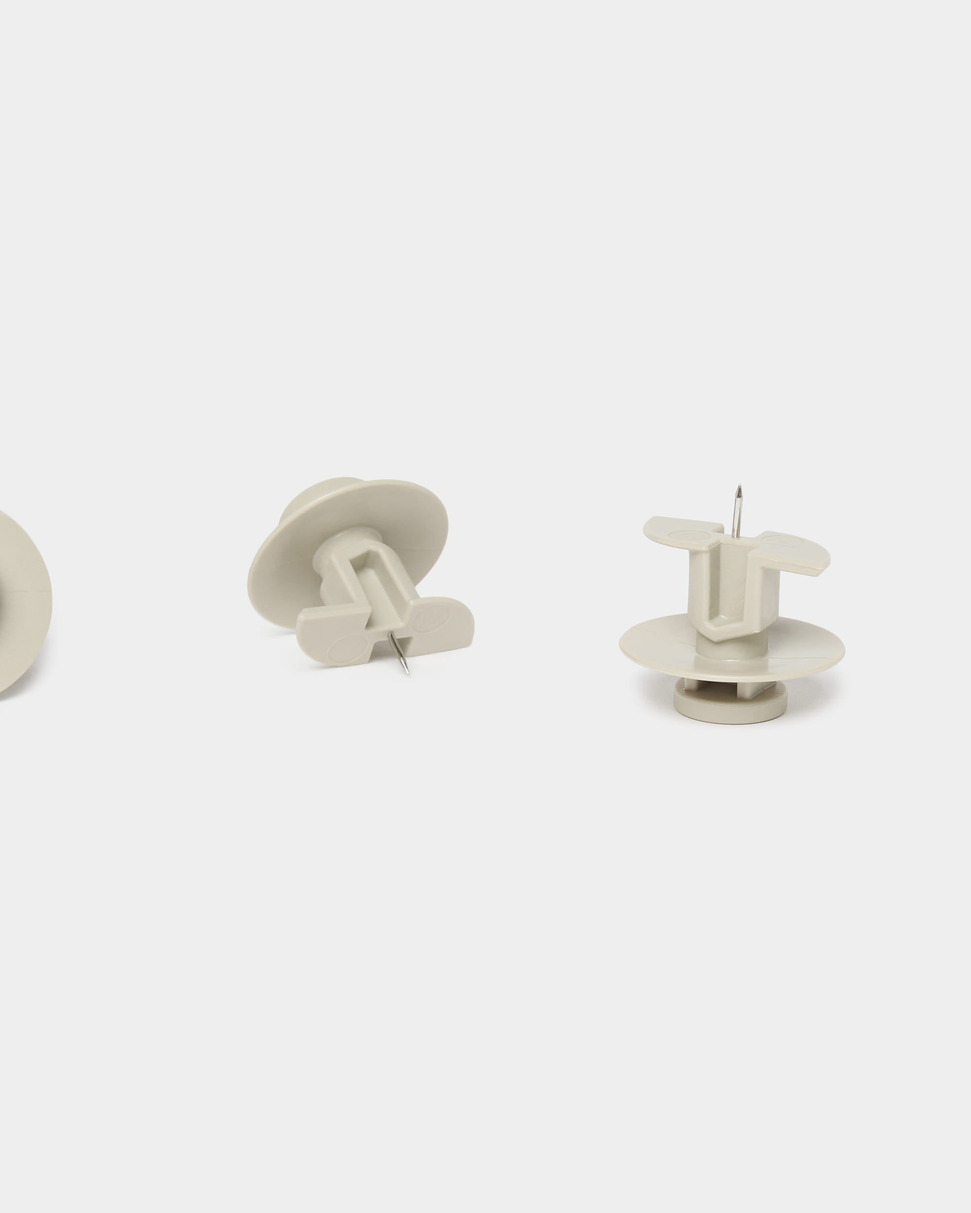 Conjunto de três alfinetes WoodUpp Dupps em tom bege e uma ferramenta, concebidos para os painéis acústicos Akupanel, apresentados na vertical e de lado sobre um fundo branco liso.