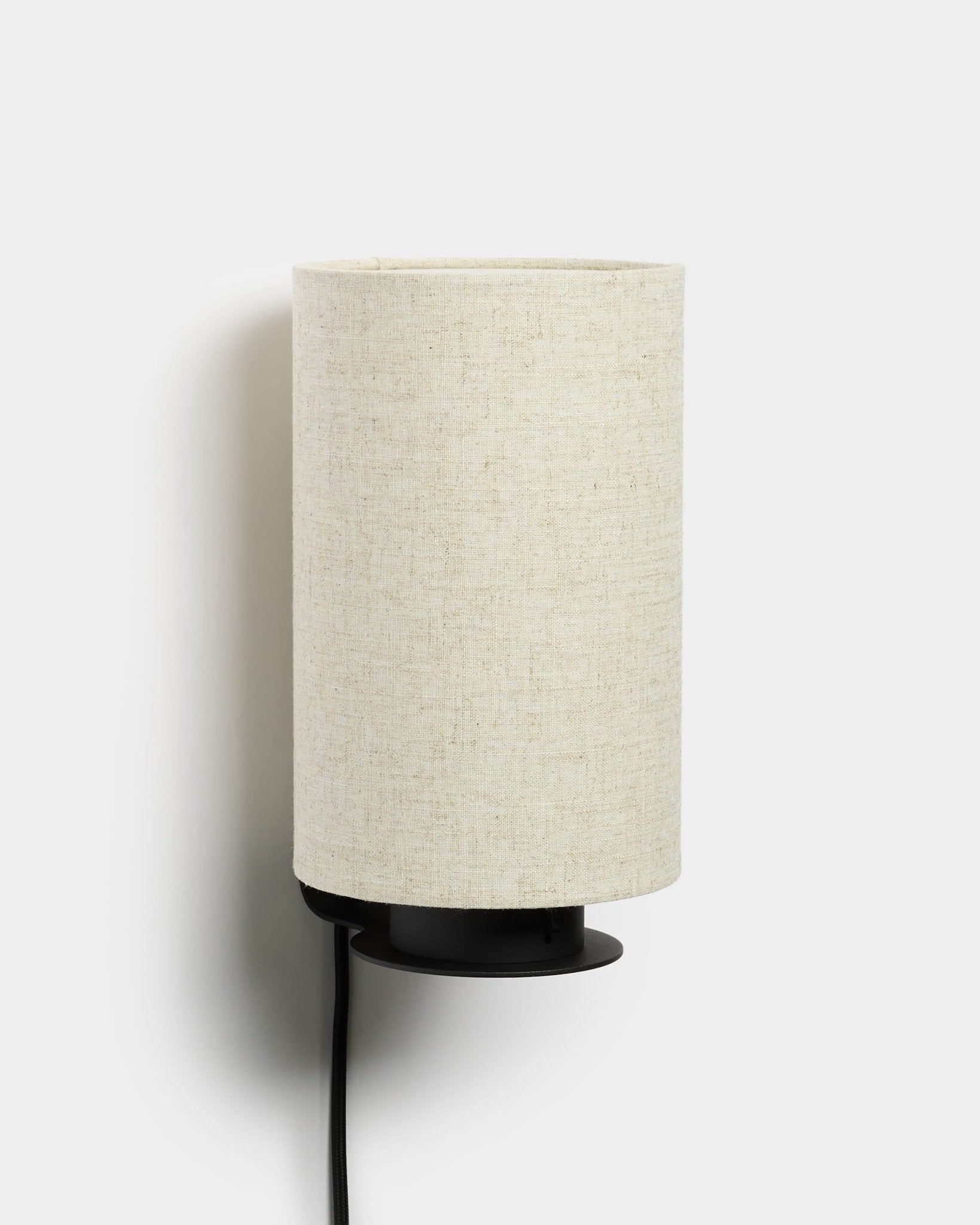 Candeeiro de parede Feya da WoodUpp com base metálica em black, abajur texturado em linho e algodão em beige e cabo de alimentação visível em black. Design nórdico minimalista.
