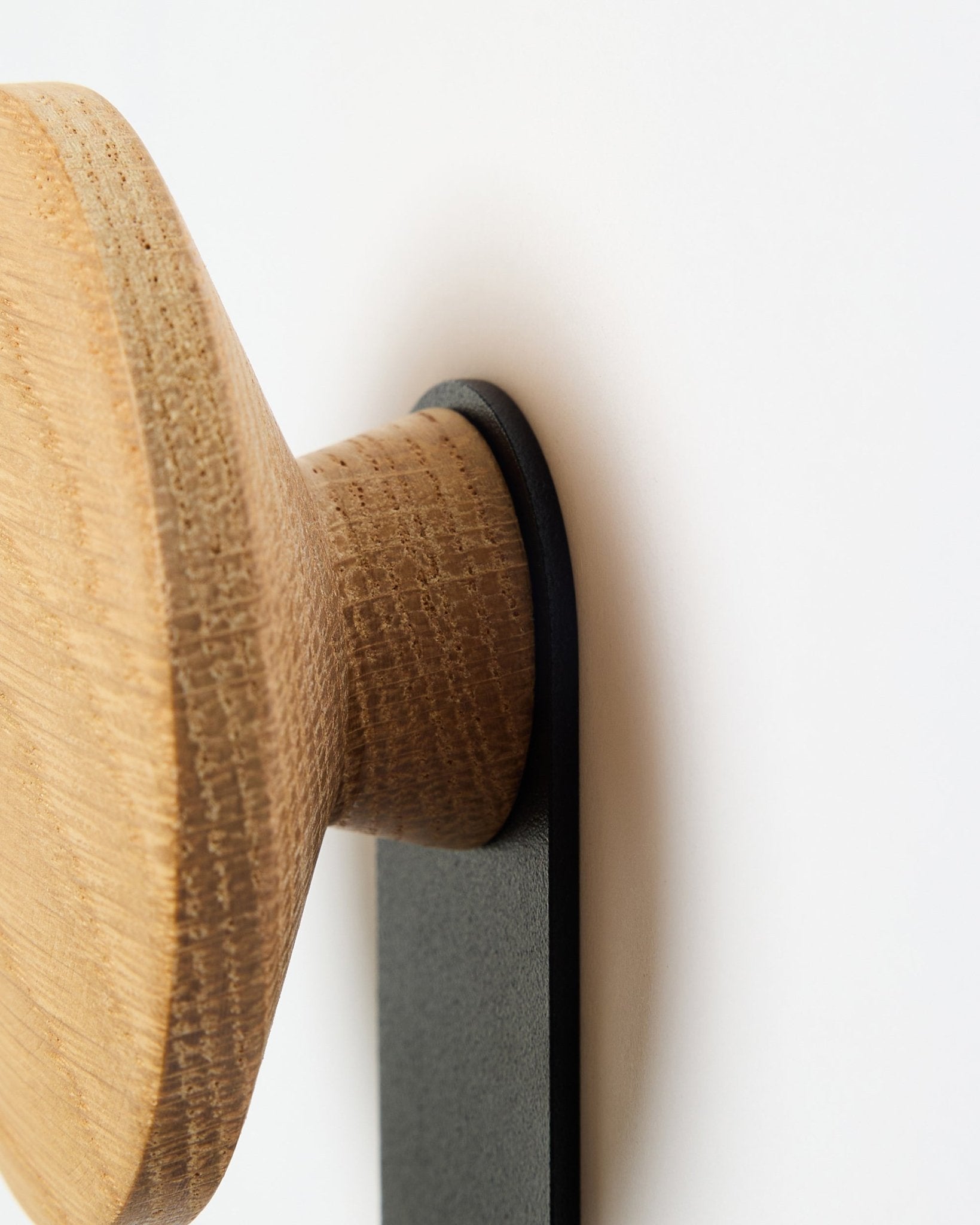 Pormenor do cabide Linn Vertical em natural oak da WoodUpp, um acessório com botão redondo de madeira montado num suporte em black, concebido para painéis acústicos Akupanel.