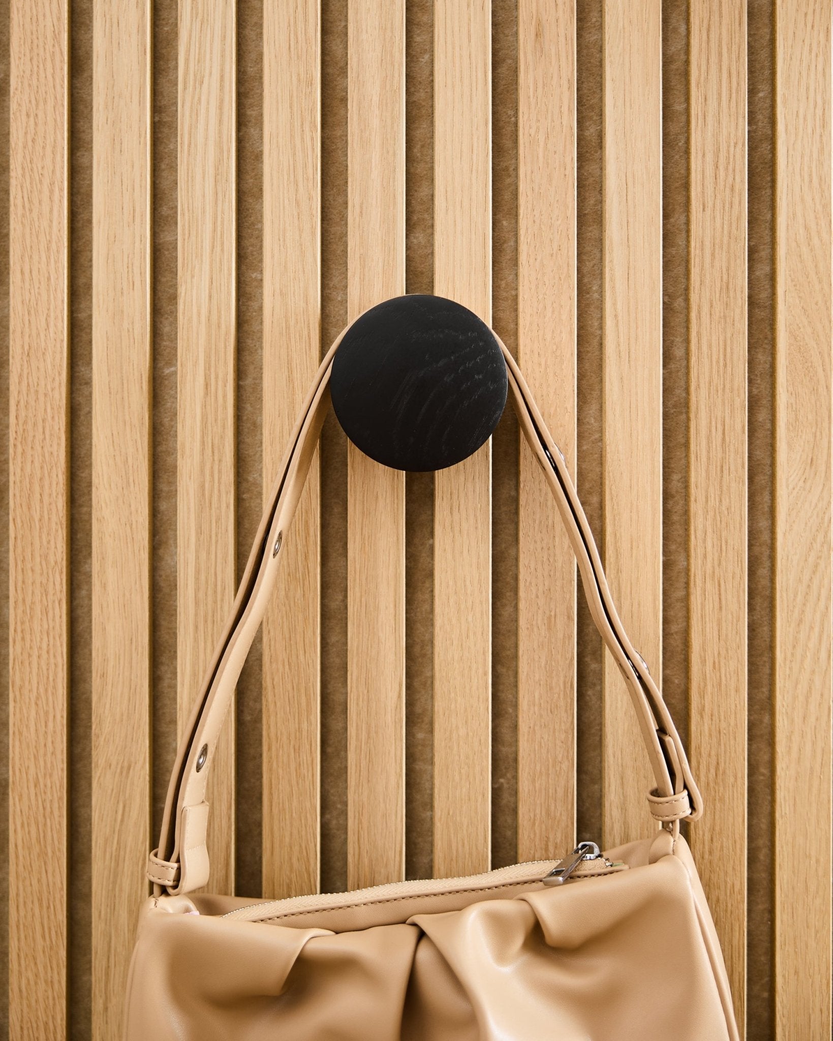 Mala de mão Beige pendurada num Linn | Single Hanger da WoodUpp em Black Oak, montado num painel acústico ripado Akupanel em madeira clara.