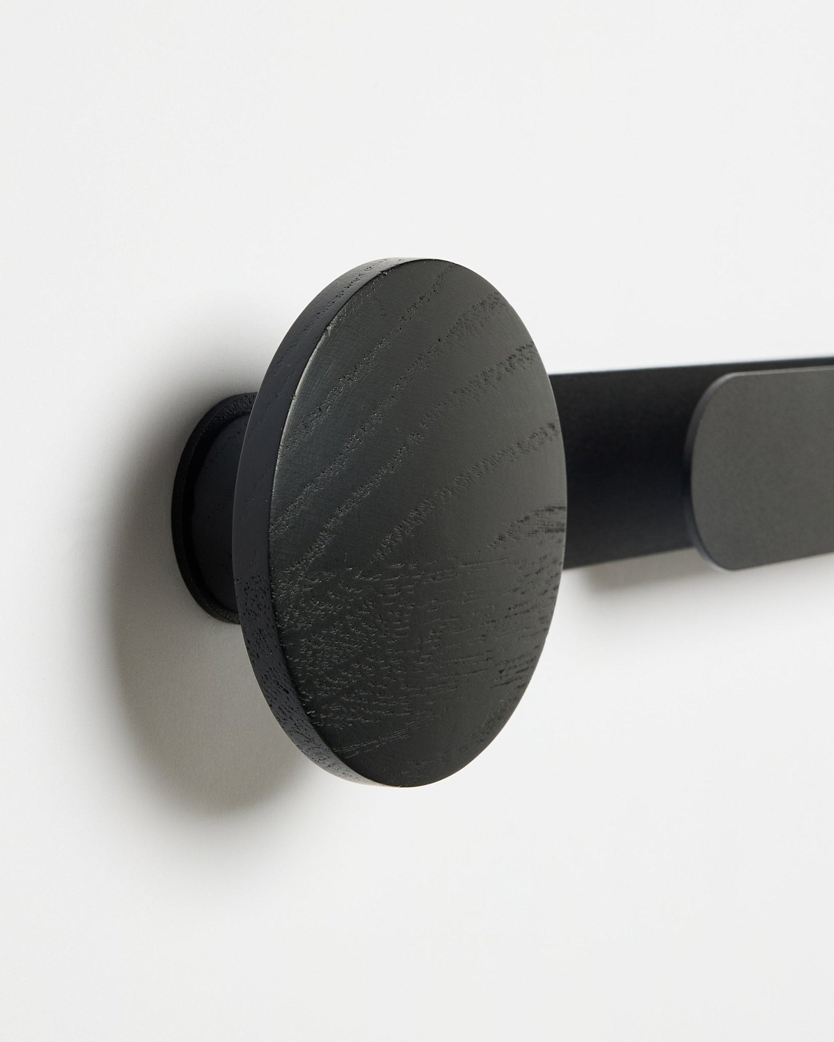 Plano aproximado do cabide WoodUpp Linn | Horizontal em Black Oak, acabamento mate black, montado numa parede branca; acessório para painéis acústicos de madeira.