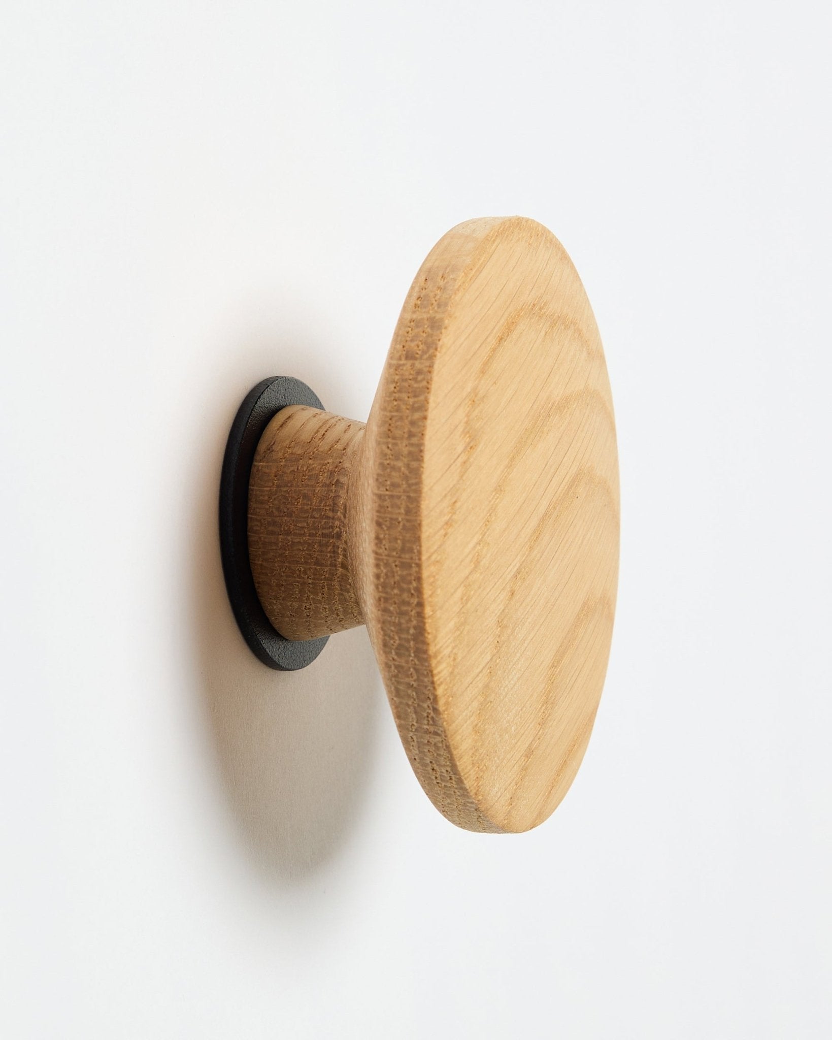 WoodUpp Linn I Single Hanger em natural oak, um gancho de parede redondo com base em black, concebido como acessório para montagem em painéis acústicos de madeira Akupanel.