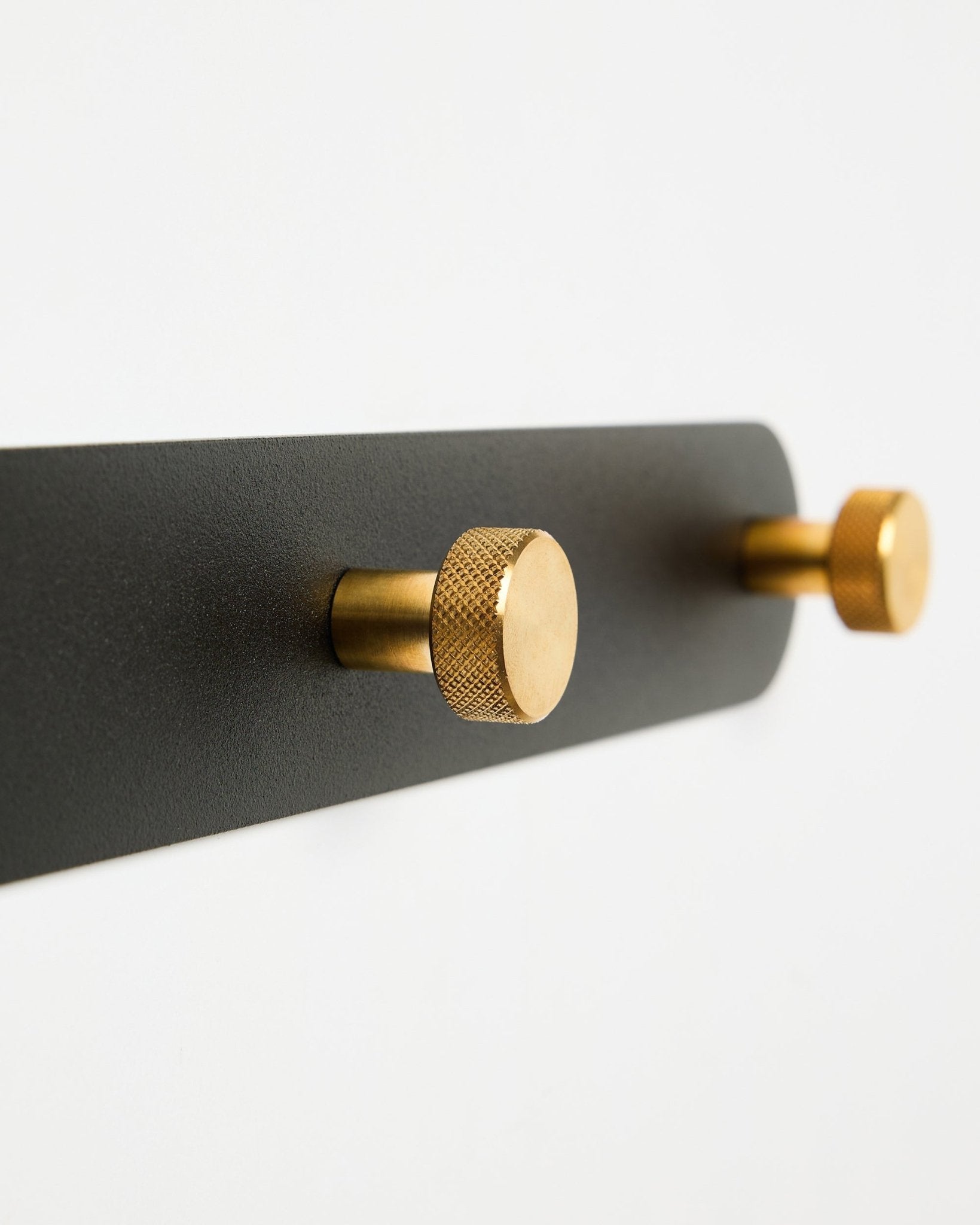 Bengaleiro Coat Hook Rack da WoodUpp Norr, modelo X7, com dois ganchos cilíndricos black e brass numa base black, apresentado sobre fundo branco.