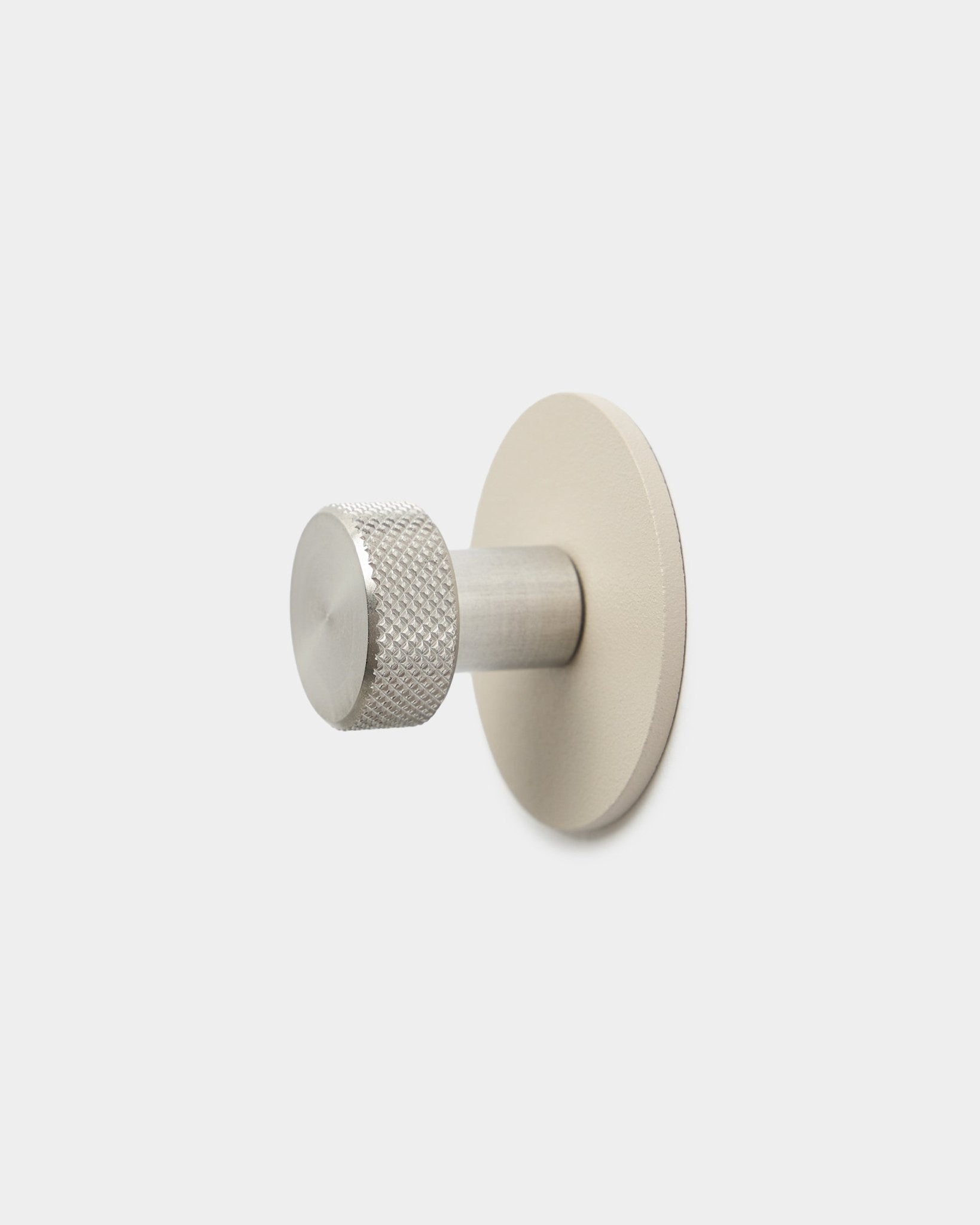 Cabide WoodUpp Norr em beige e steel inoxidável, com extremidade cilíndrica texturada e base redonda, acessório para Akupanel, sobre um fundo branco liso.