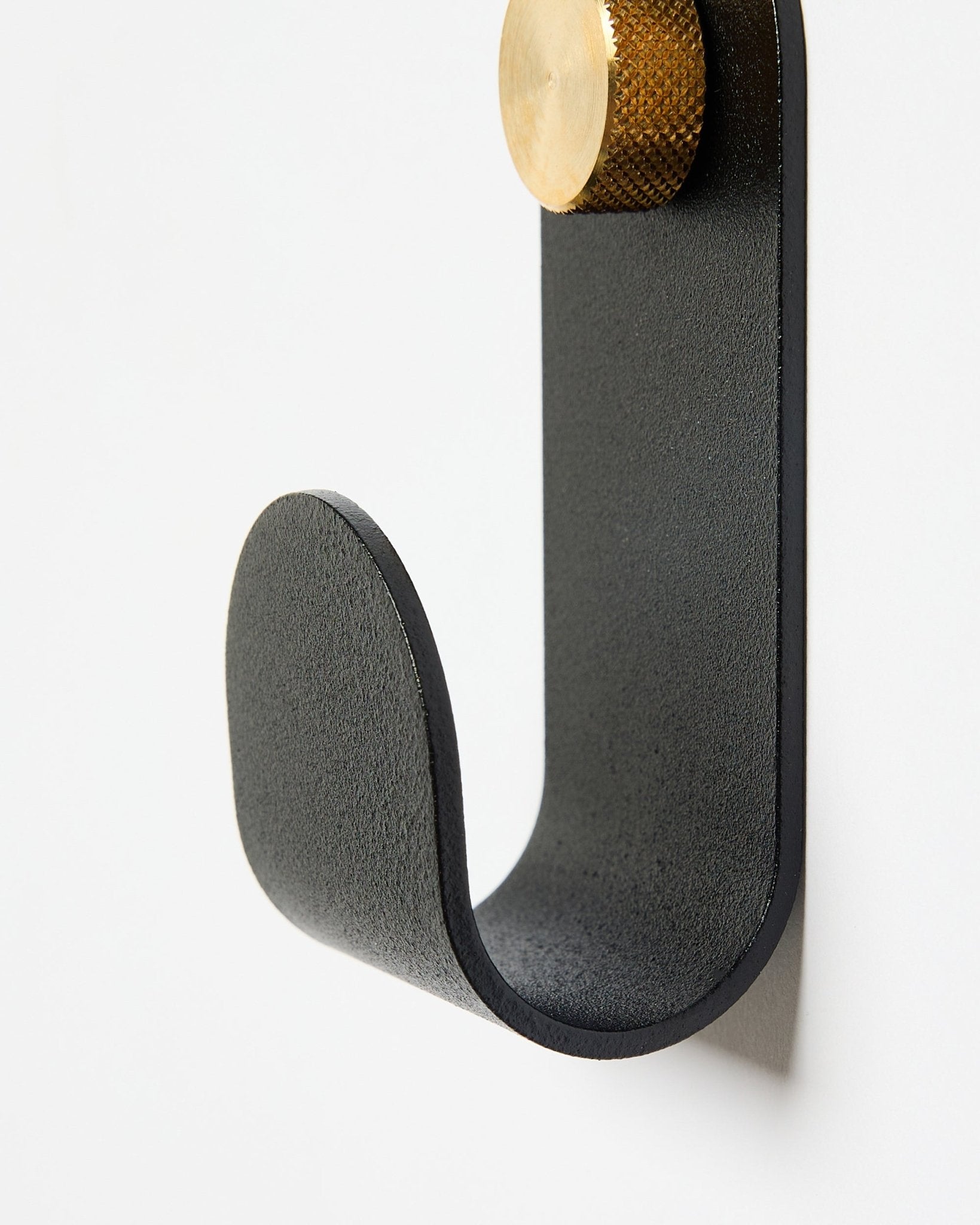 O Norr Single Hanger da WoodUpp tem um braço curvo em metal black com uma tampa dourada, pensado como acessório para usar com painéis acústicos em paredes brancas.
