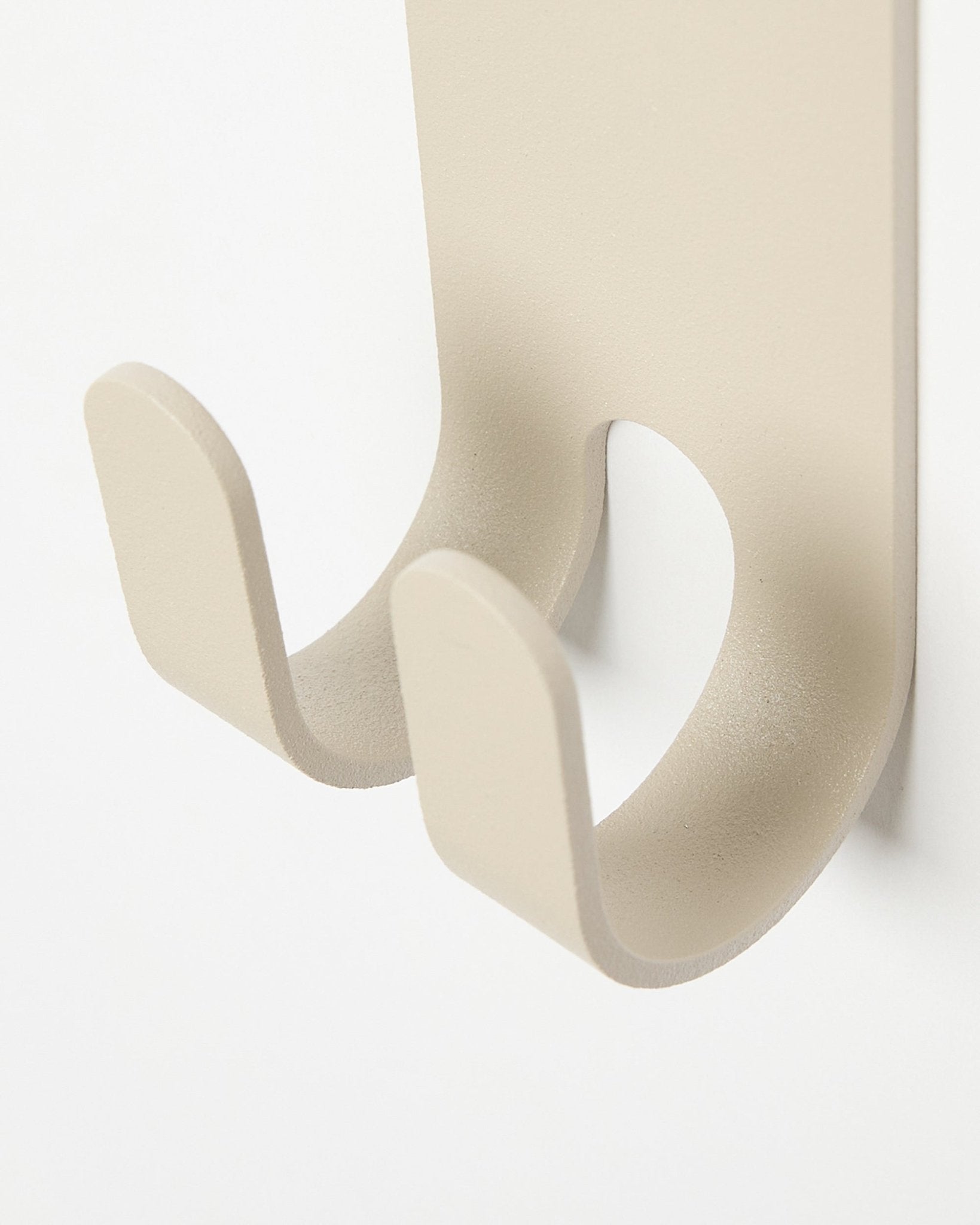 Plano aproximado do Norr Double Hanger em beige da WoodUpp, um gancho de parede metálico minimalista instalado num painel ripado colored claro Painel acústico.
