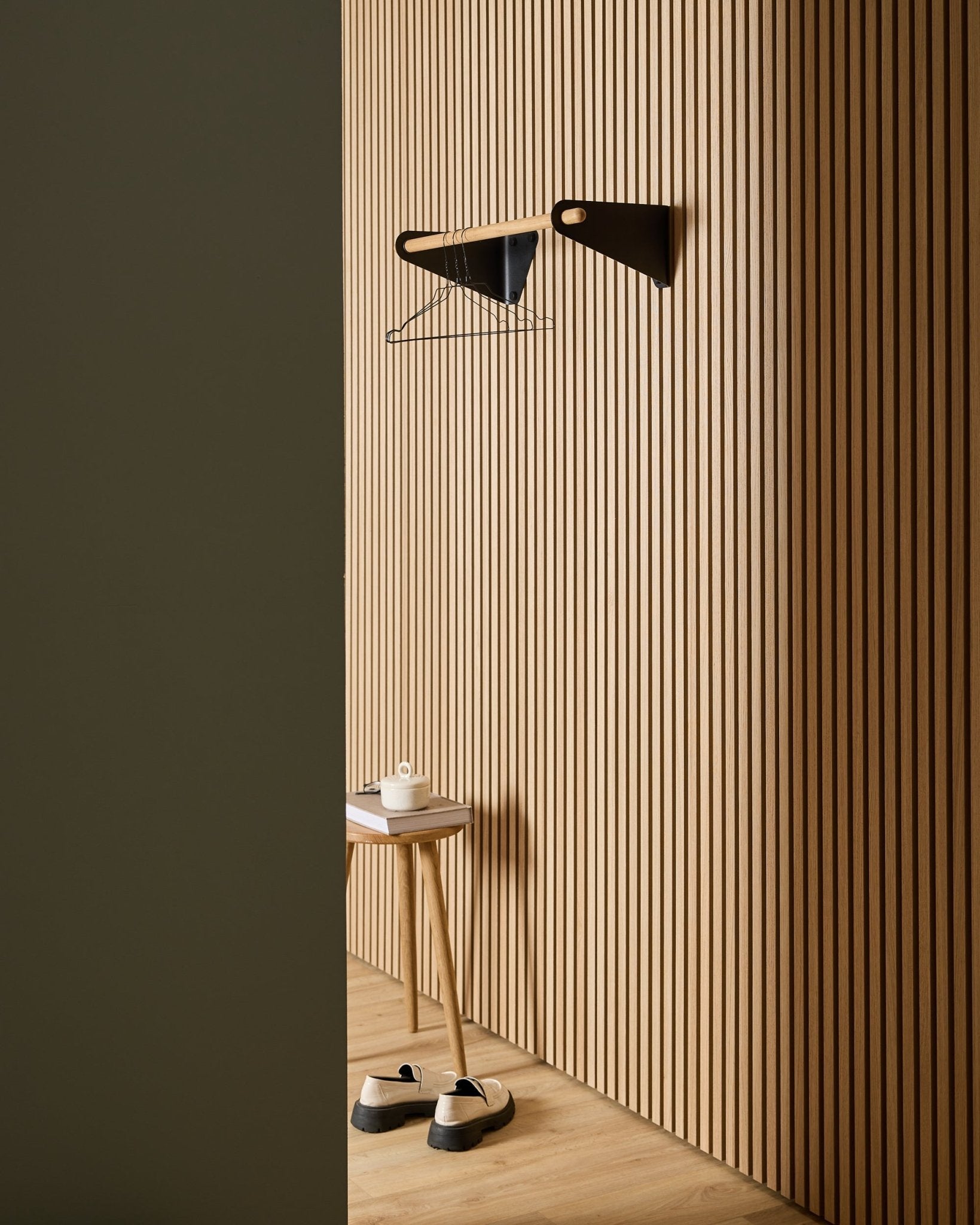 Entrada minimalista com painéis acústicos nórdicos ripados em madeira WoodUpp Akupanel, black Linn Coat Rail (75,9 cm), banco, sapatos, prateleira de parede e rolo de papel.