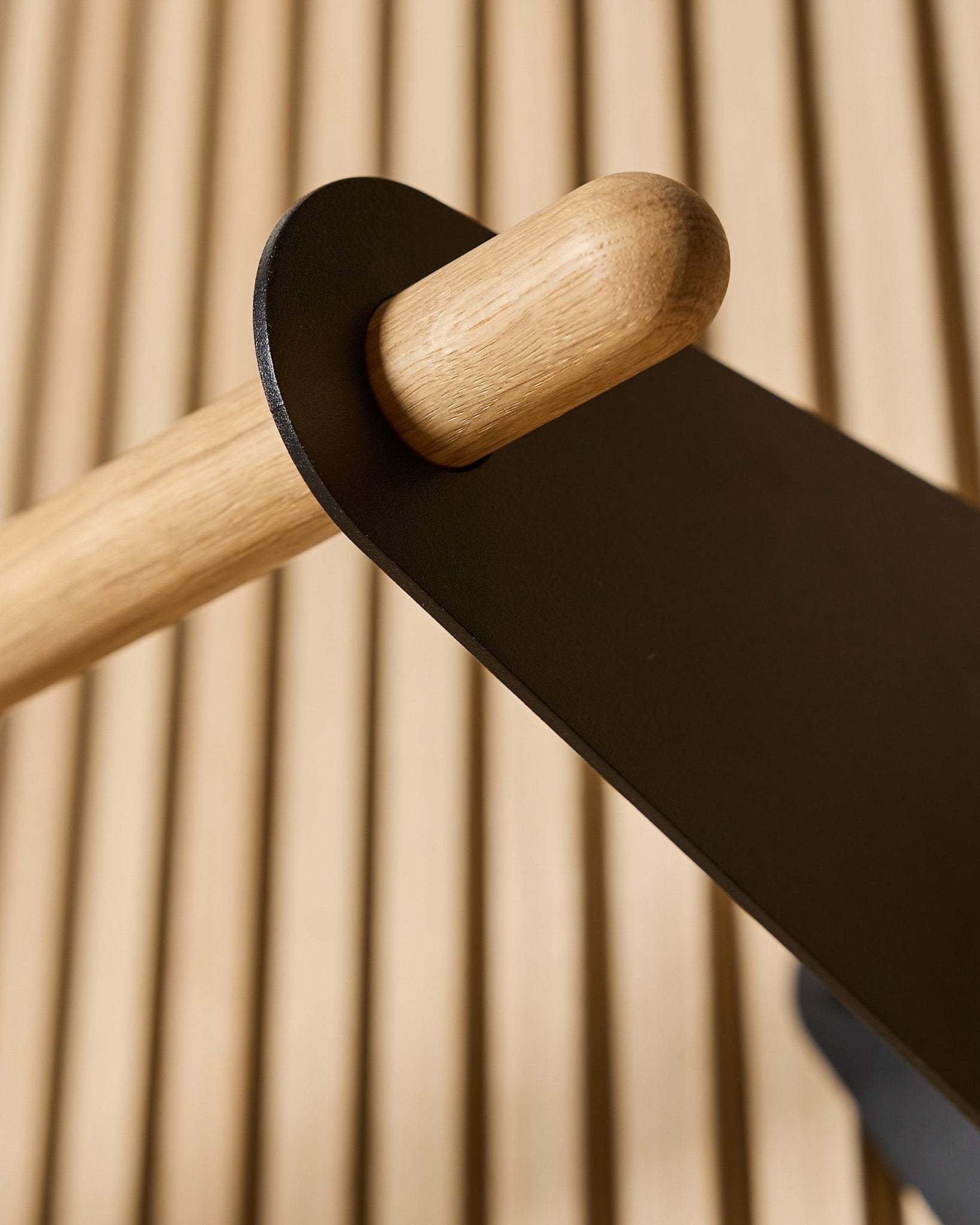 Plano aproximado do Coat Rail WoodUpp Linn em black, 75,9 cm, com um varão em carvalho maciço montado num suporte metálico black num painel acústico nórdico ripado.